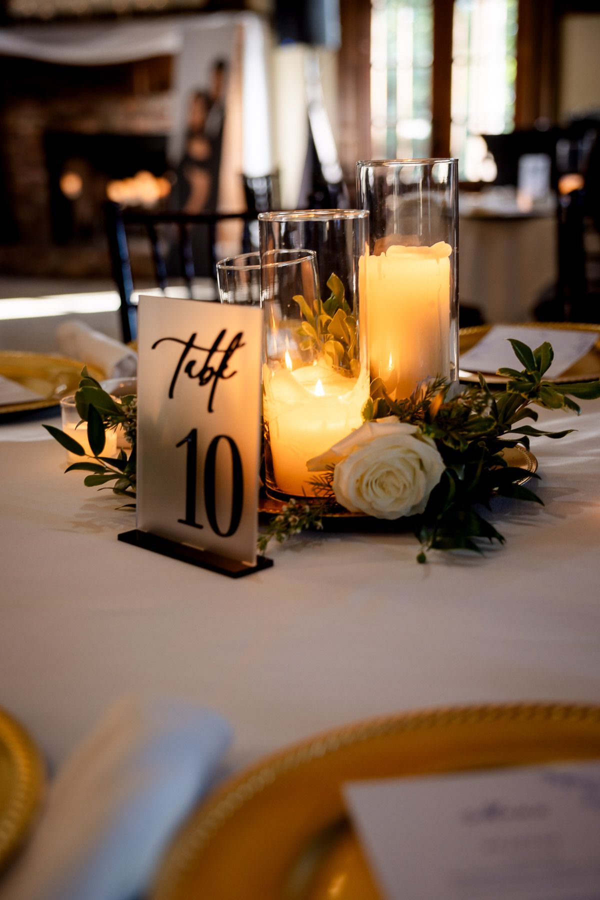 Wedding table centerpiece with glowing pillar candles, white rose, and greenery beside table number 10.
