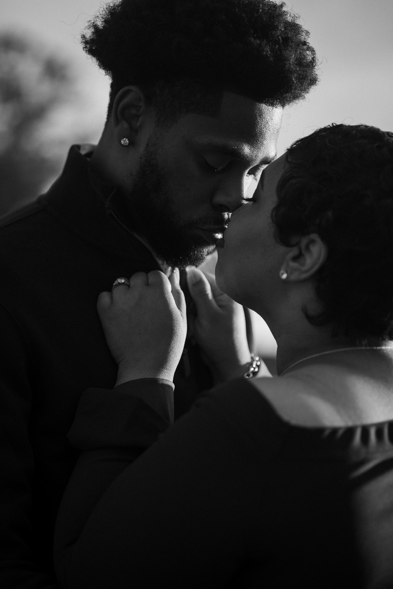 Black and white portrait of a couple sharing an intimate kiss, her hands resting on his collar, ideal for engagement or romance photography.