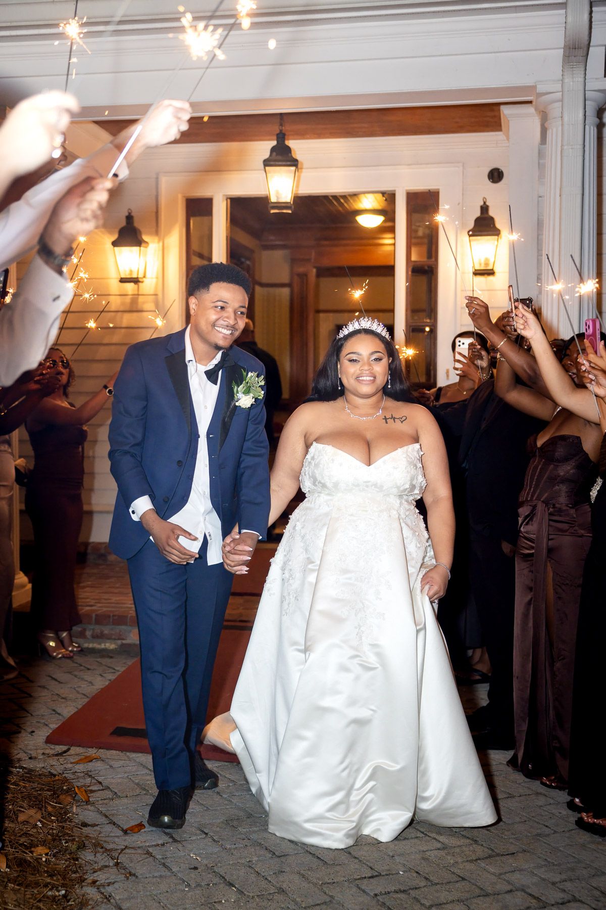 Newlywed couple exits wedding venue through sparkler send-off, bride in white gown and groom in navy suit holding hands.