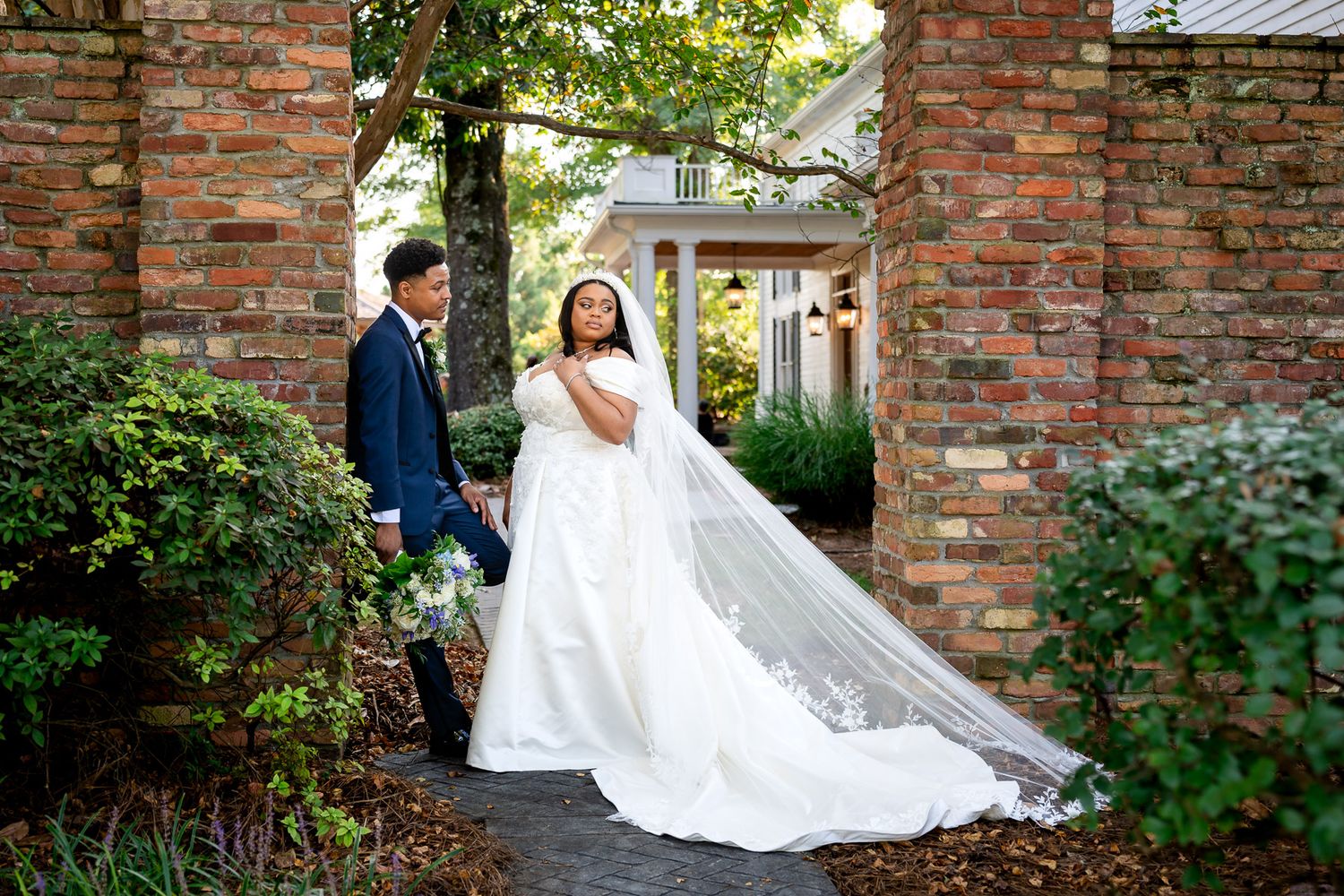 Bride in flowing white gown with long veil stands with groom in navy suit at Carl House wedding venue in Auburn Georgia