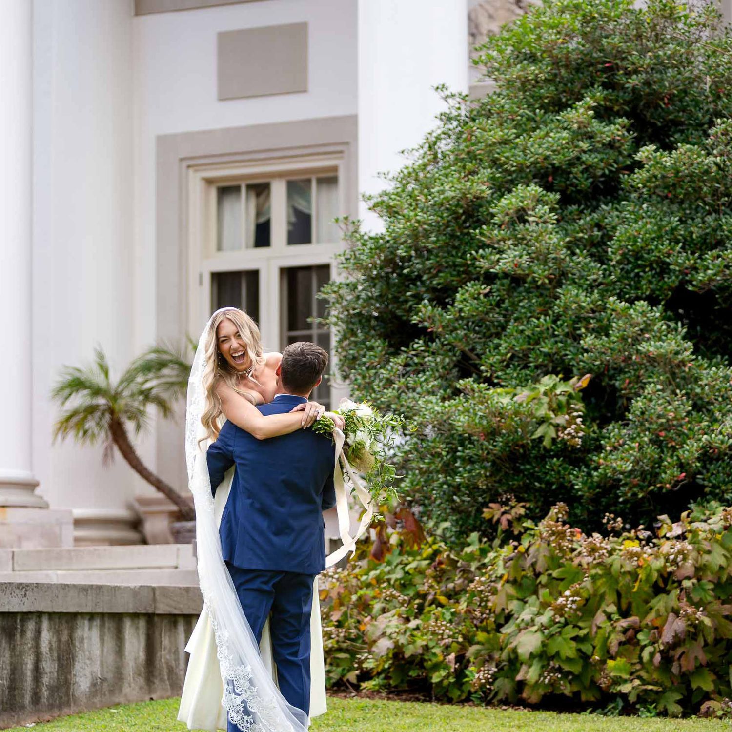 Groom in navy suit lifts bride in white gown and veil outside their wedding in la grange Georgia