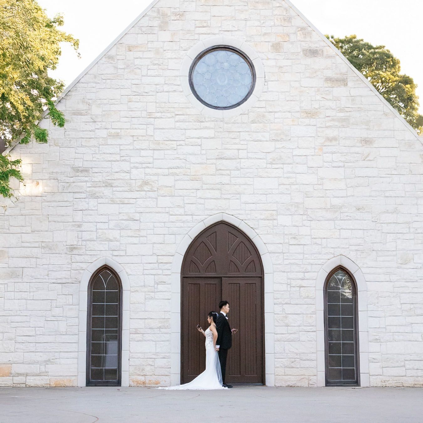 Classic white stone church with arched wooden doors, round window, and gothic style windows framing the entrance.