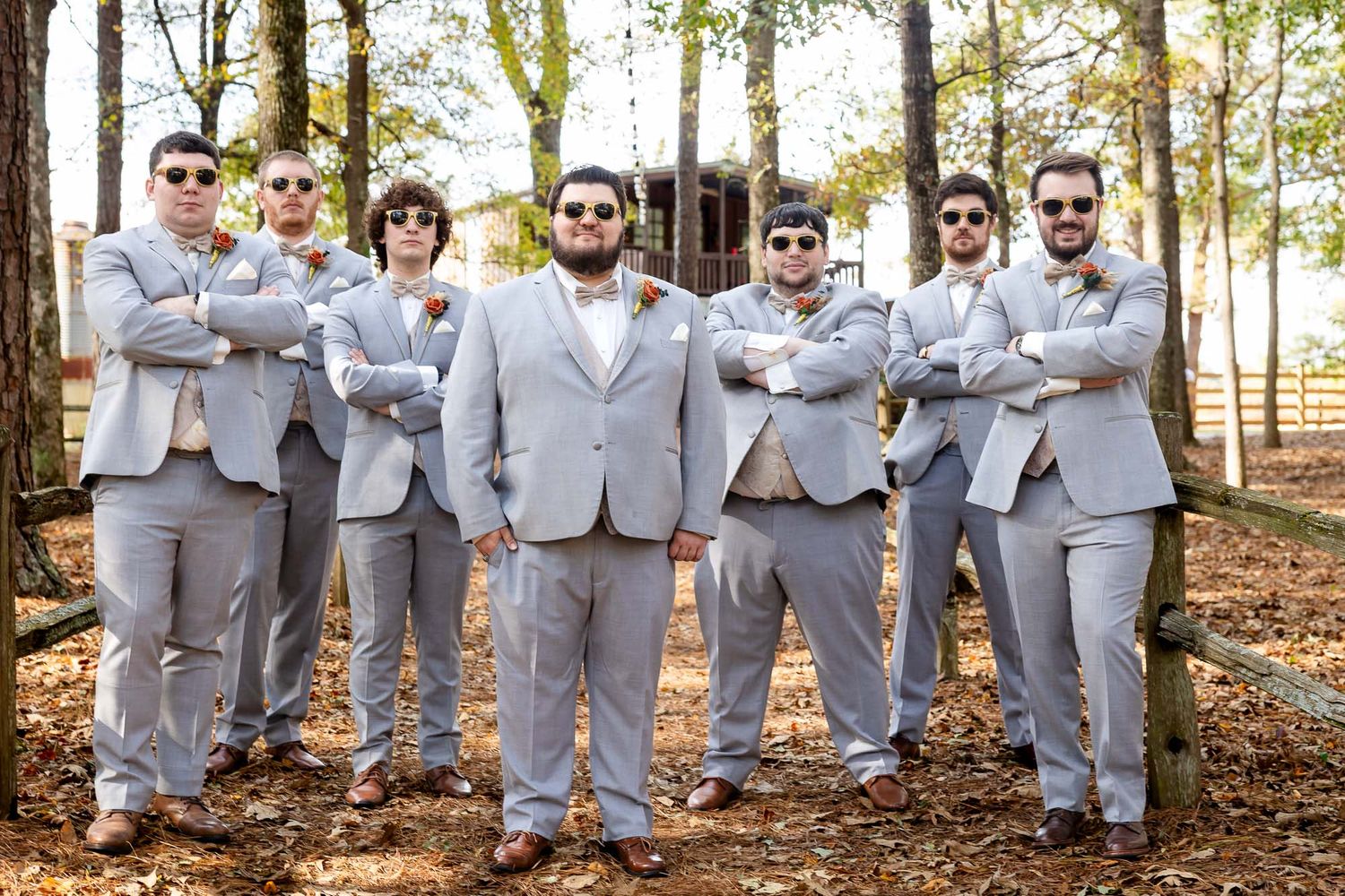 Groomsmen in matching gray suits and sunglasses pose with arms crossed outdoors at wedding.