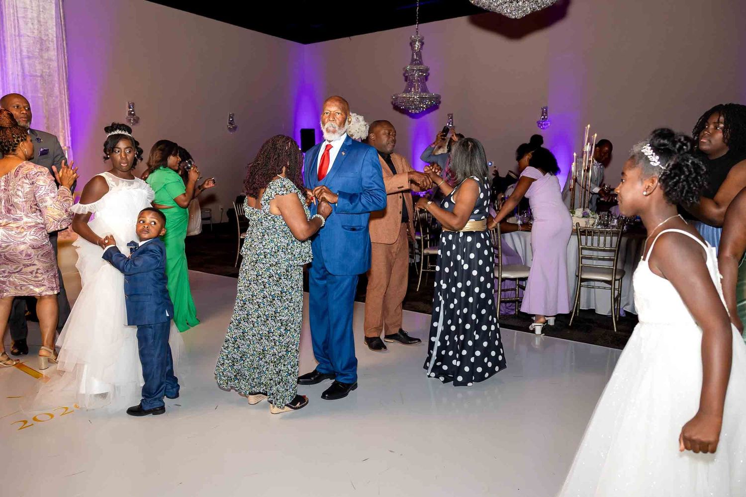 Joyful wedding guests dance together on white dance floor during lively reception celebration.
