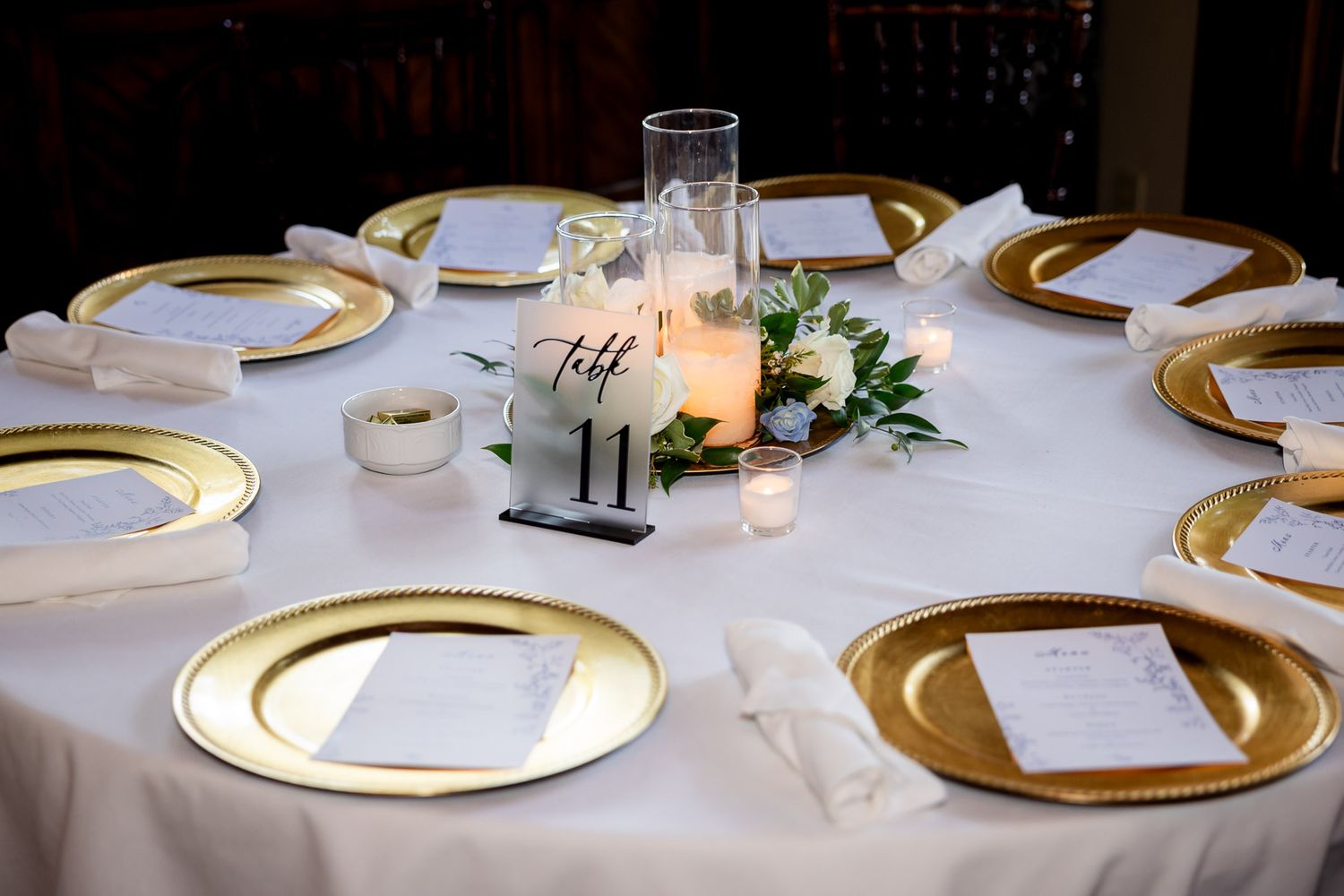 Elegant wedding reception table with gold charger plates, white linens, candle centerpiece, and table number 11.
