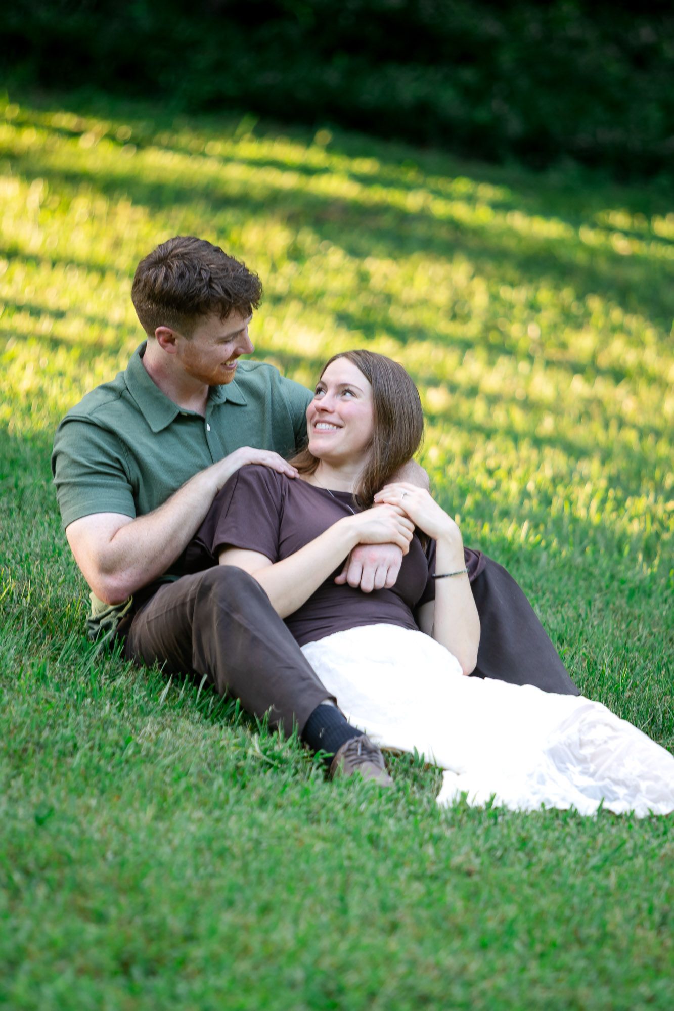 Happy couple relaxing on green grass in a sunny park, woman smiling up at man in a tender romantic moment.