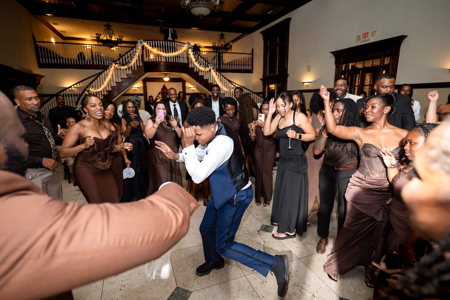 Guests dancing joyfully at an elegant wedding reception with warm lighting and decorative arch backdrop.