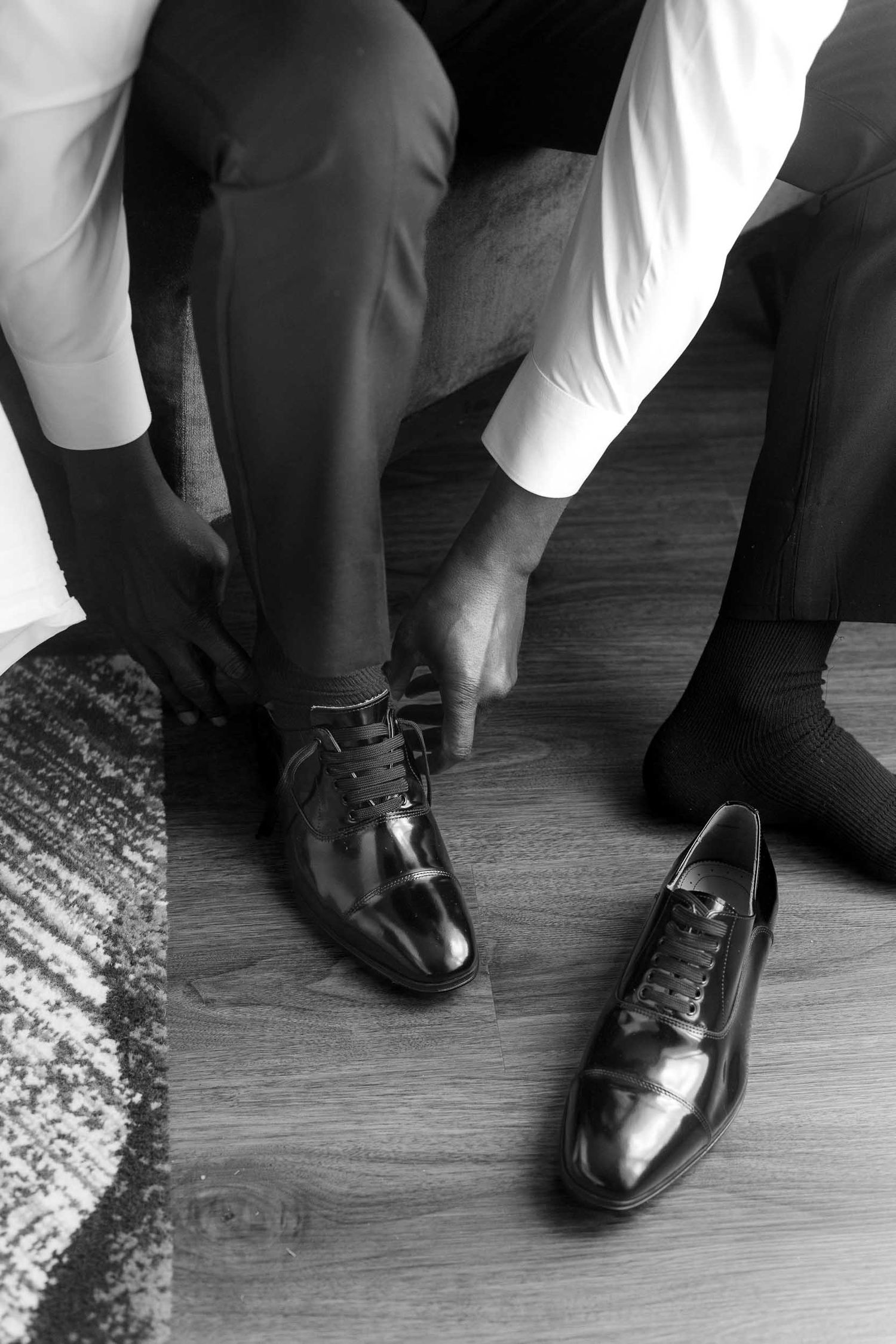 Black and white photo of a groom tying his dress shoes before wedding ceremony.