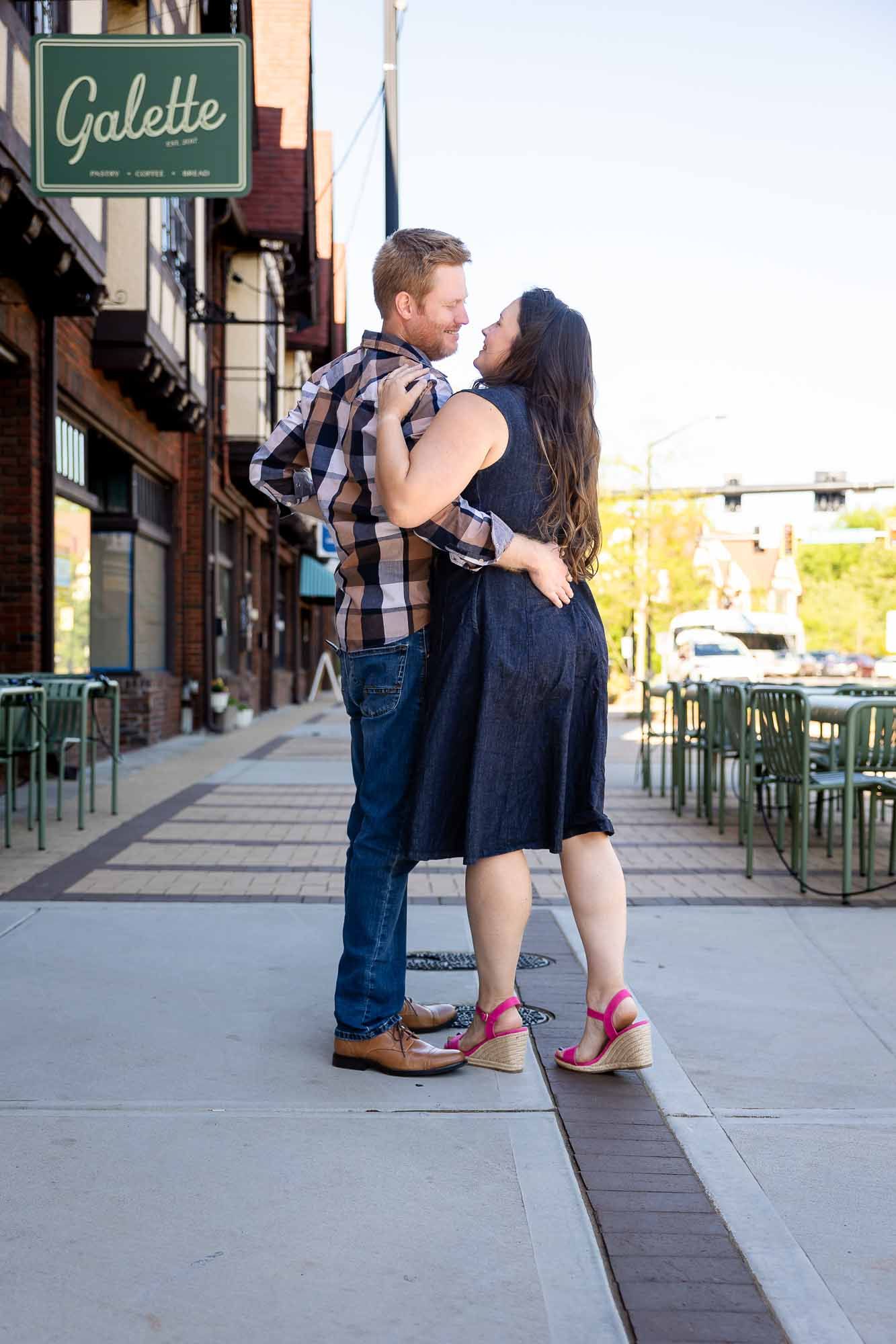 Couple sharing a romantic kiss on a city sidewalk outside Galette restaurant during engagement photo session.