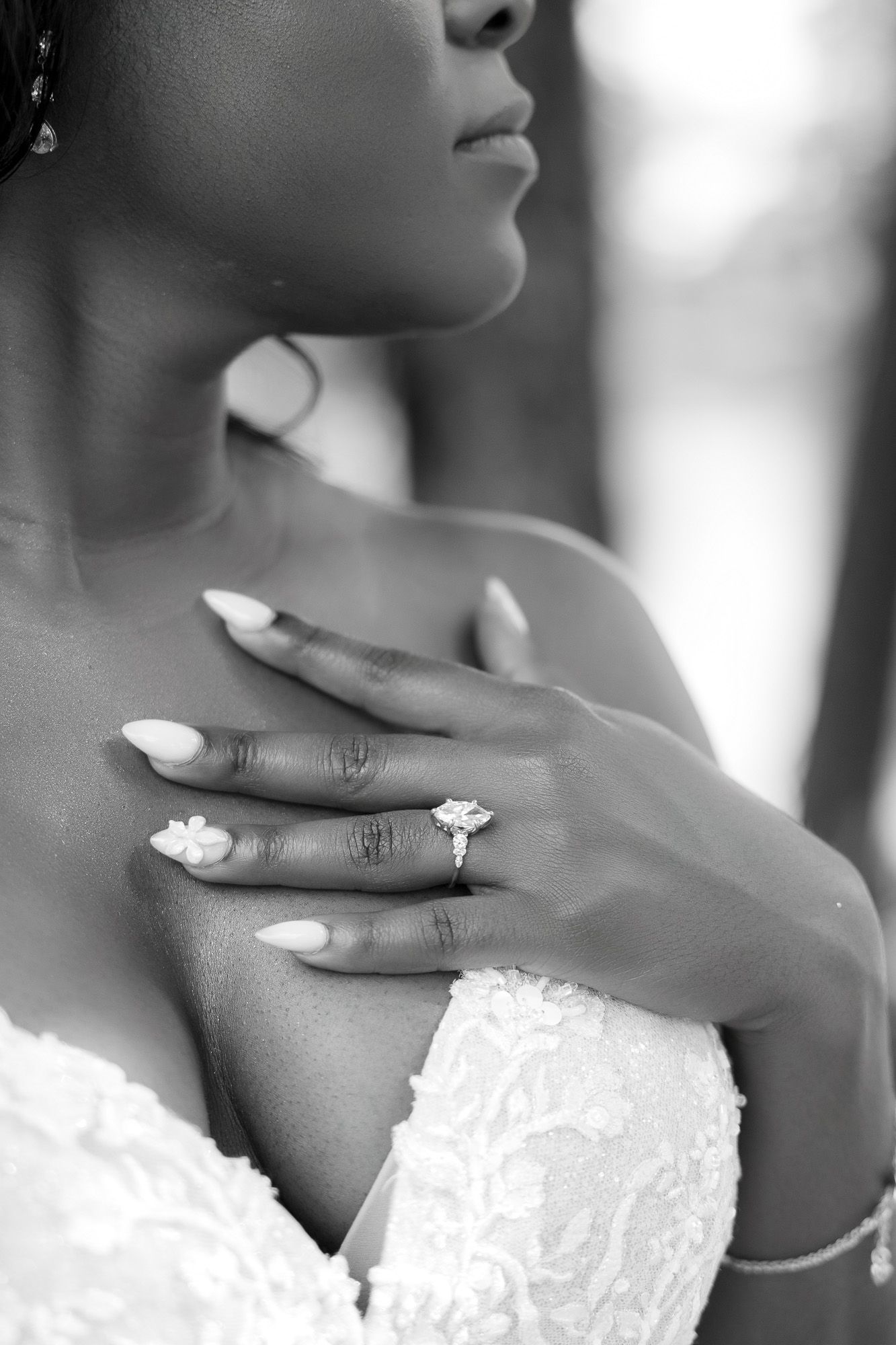 Black and white photo of a bride in lace gown showcasing her diamond engagement ring with manicured nails.
