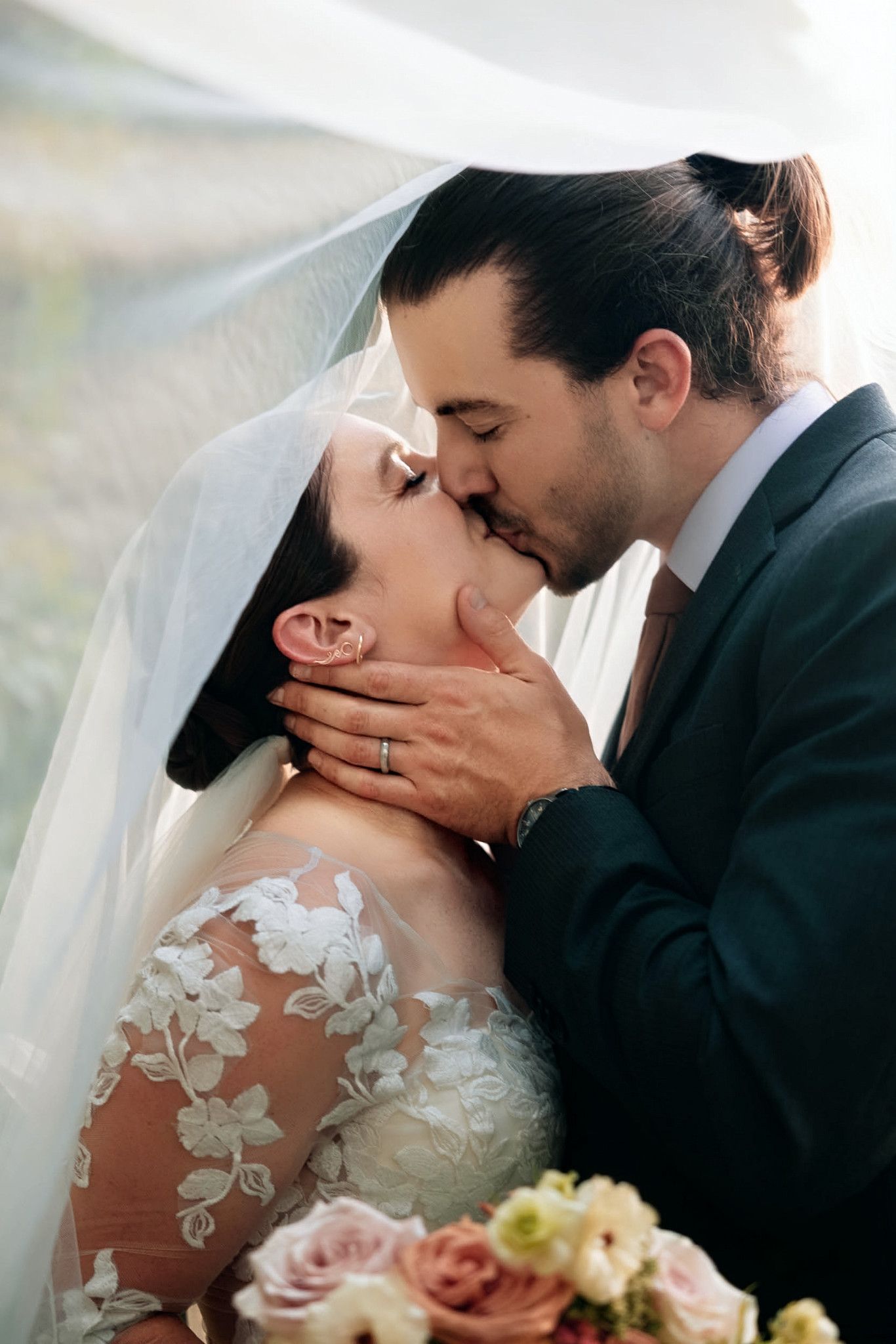 A bride and groom share a romantic kiss under a flowing veil, surrounded by soft floral details on her lace wedding dress in atlanta georgia