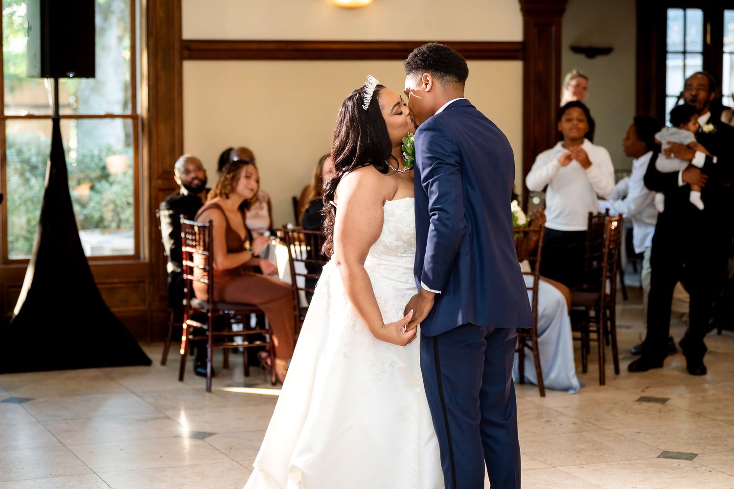 A bride and groom share their first dance at an elegant wedding reception with guests seated in the background.