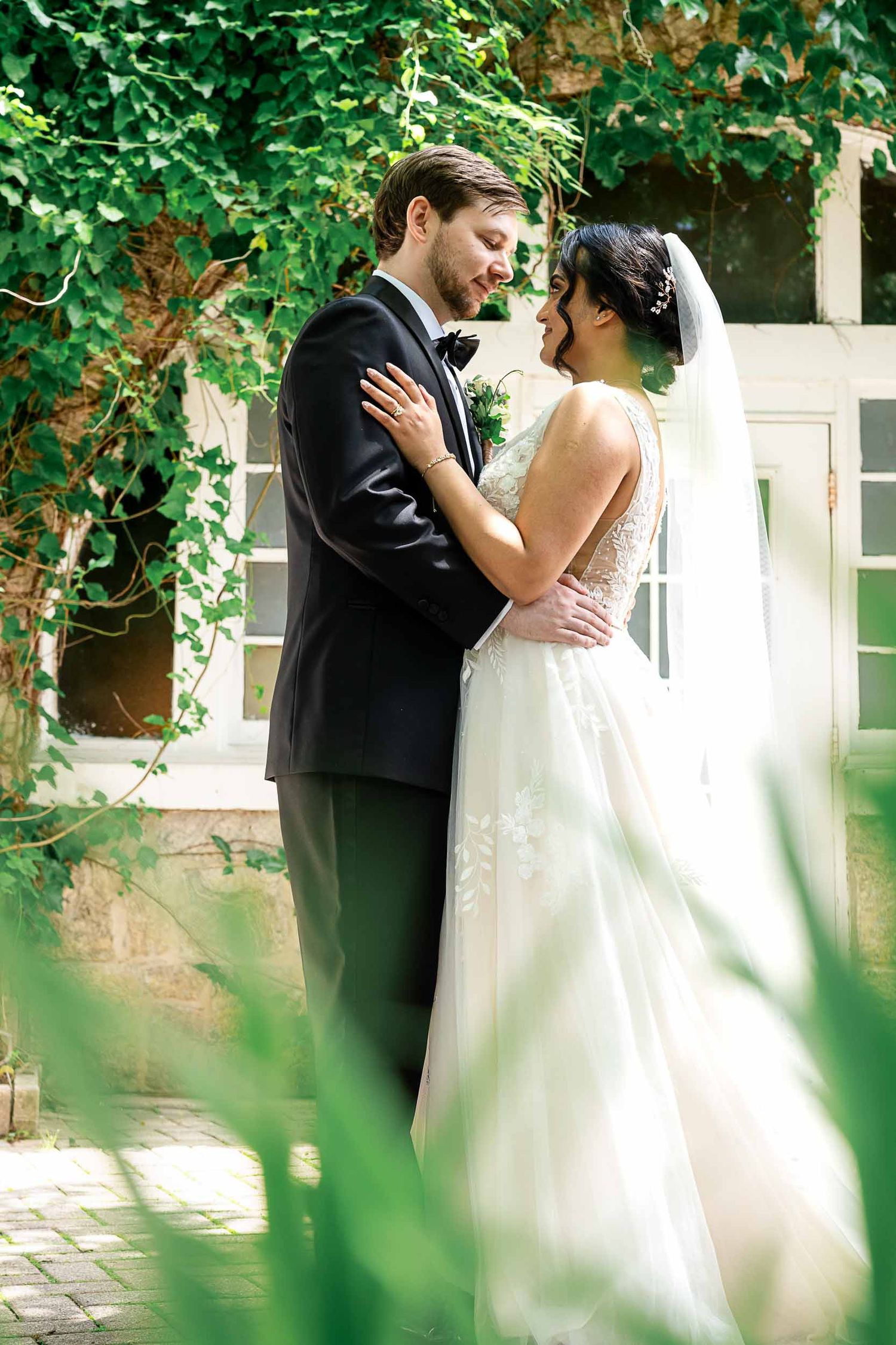 A bride and groom share a romantic moment in a lush garden, with ivy-covered walls framing their elegant wedding attire.