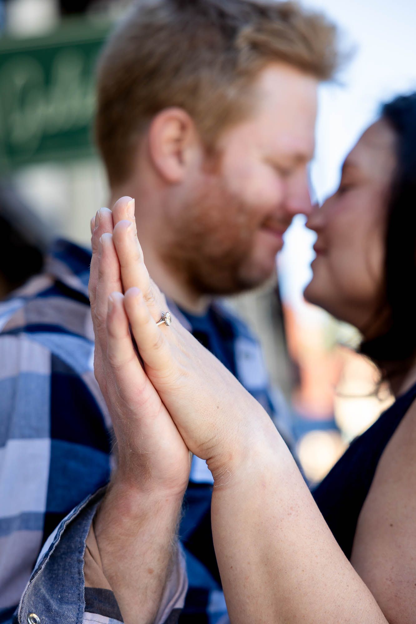 Close-up of engaged couple holding hands showing diamond ring while sharing a tender moment outdoors.