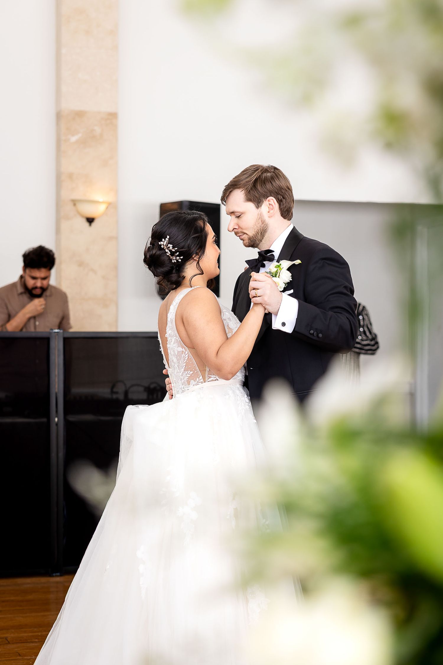 Bride and groom share their first dance, with groom in black tuxedo and bride in white ballgown at wedding reception.