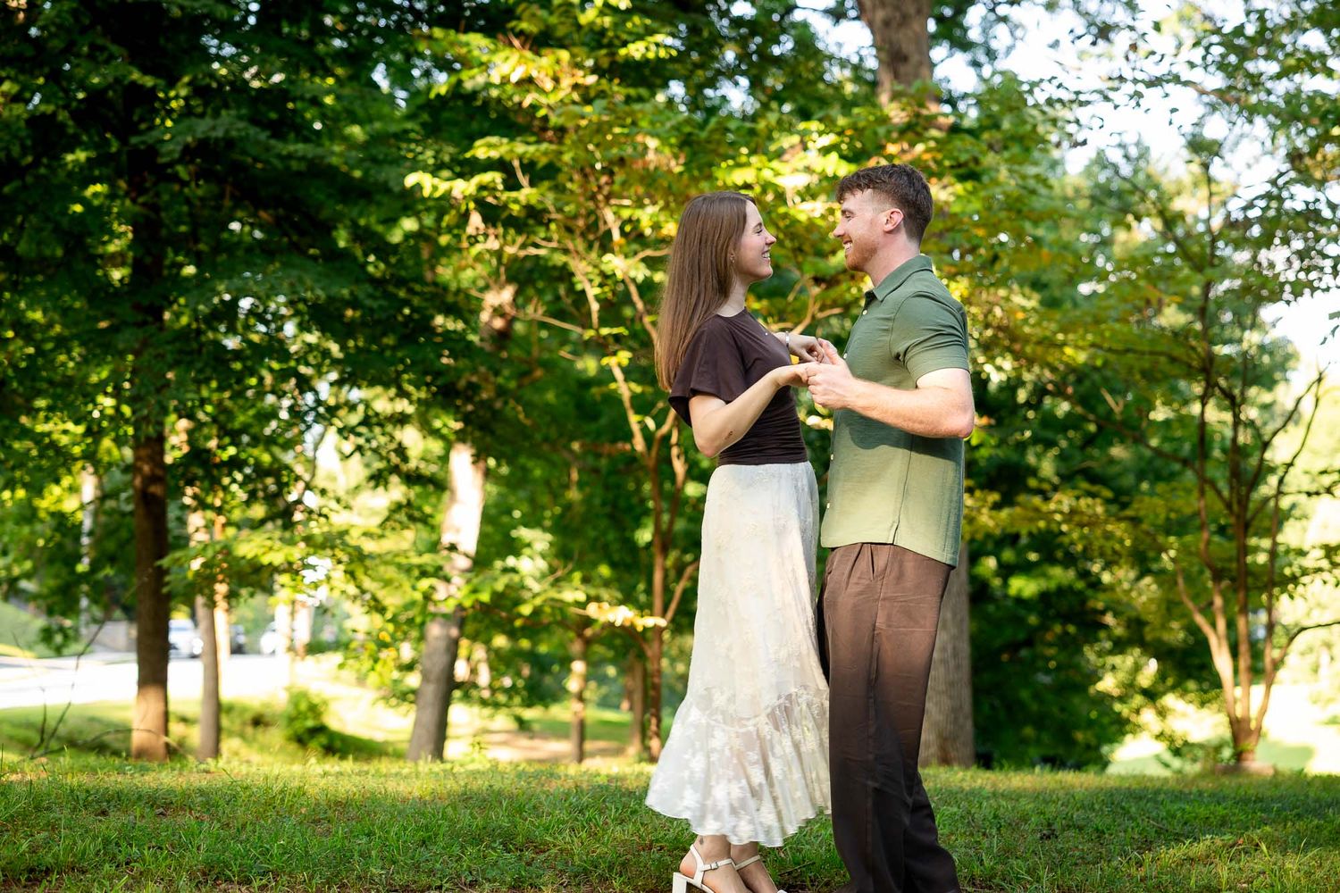 Couple dancing together in a lush green park, holding hands and smiling on a sunny day.