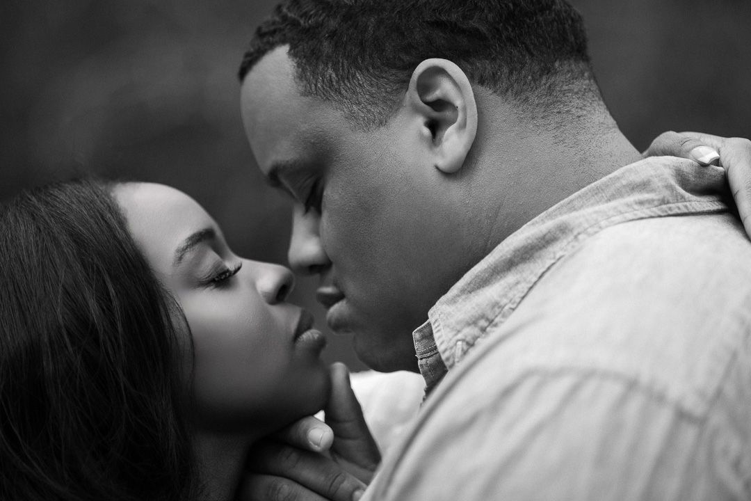 Black and white photo of a romantic couple sharing a tender kiss in an intimate close-up portrait.