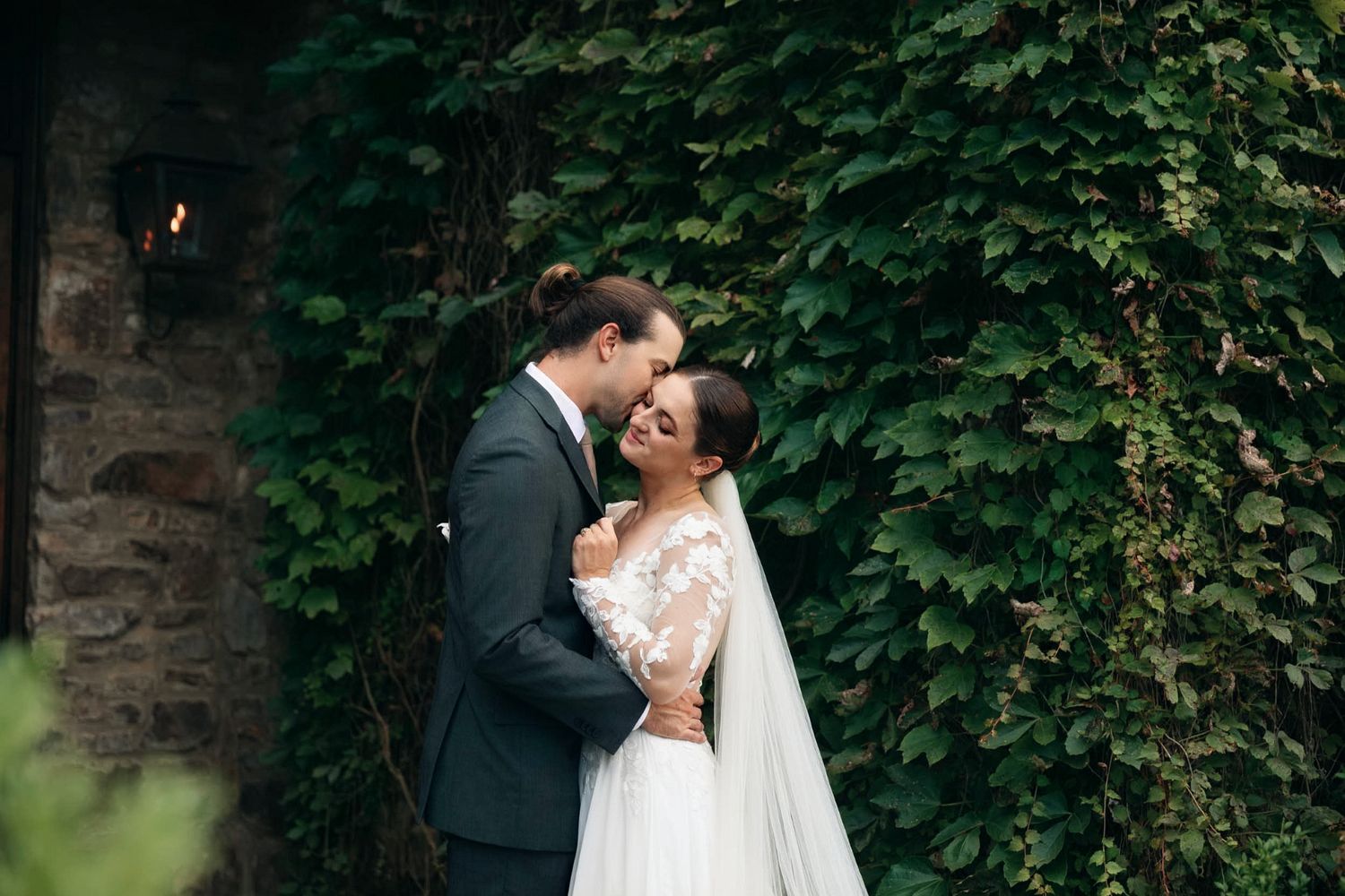 A bride and groom share a romantic moment surrounded by lush green ivy walls on their wedding day.