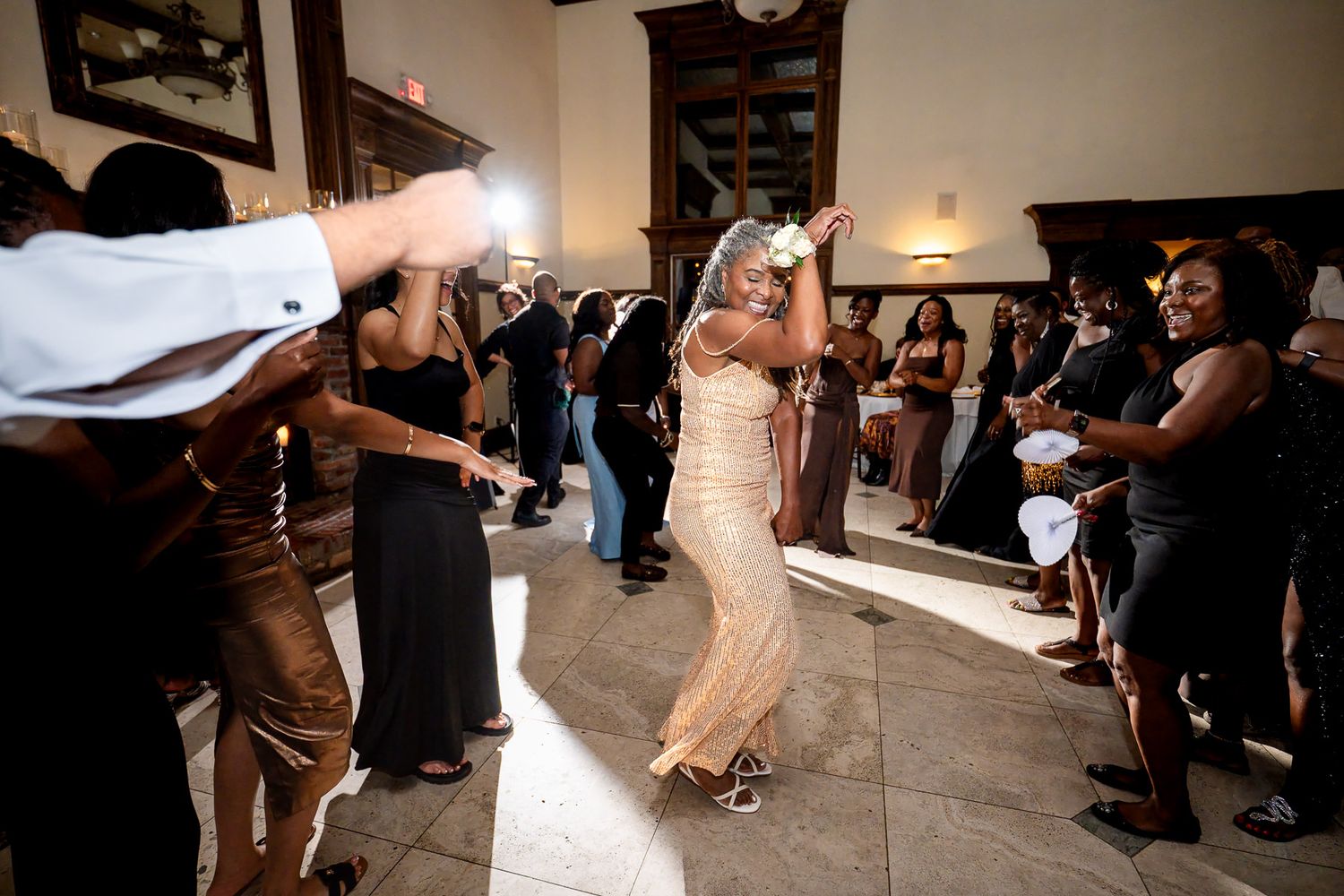 Bride in a gold dress dancing joyfully surrounded by guests at a lively wedding reception celebration.
