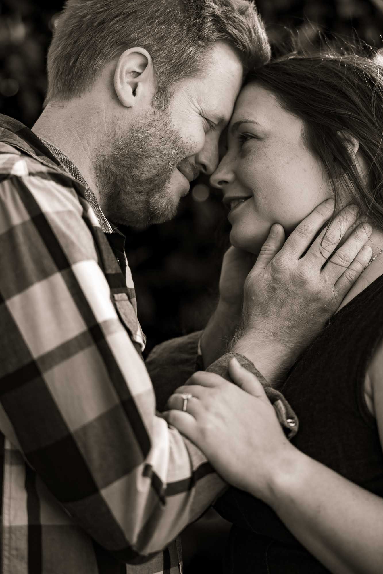 Black and white photo of a romantic couple sharing an intimate moment, man gently holding womans face as they lean close together.