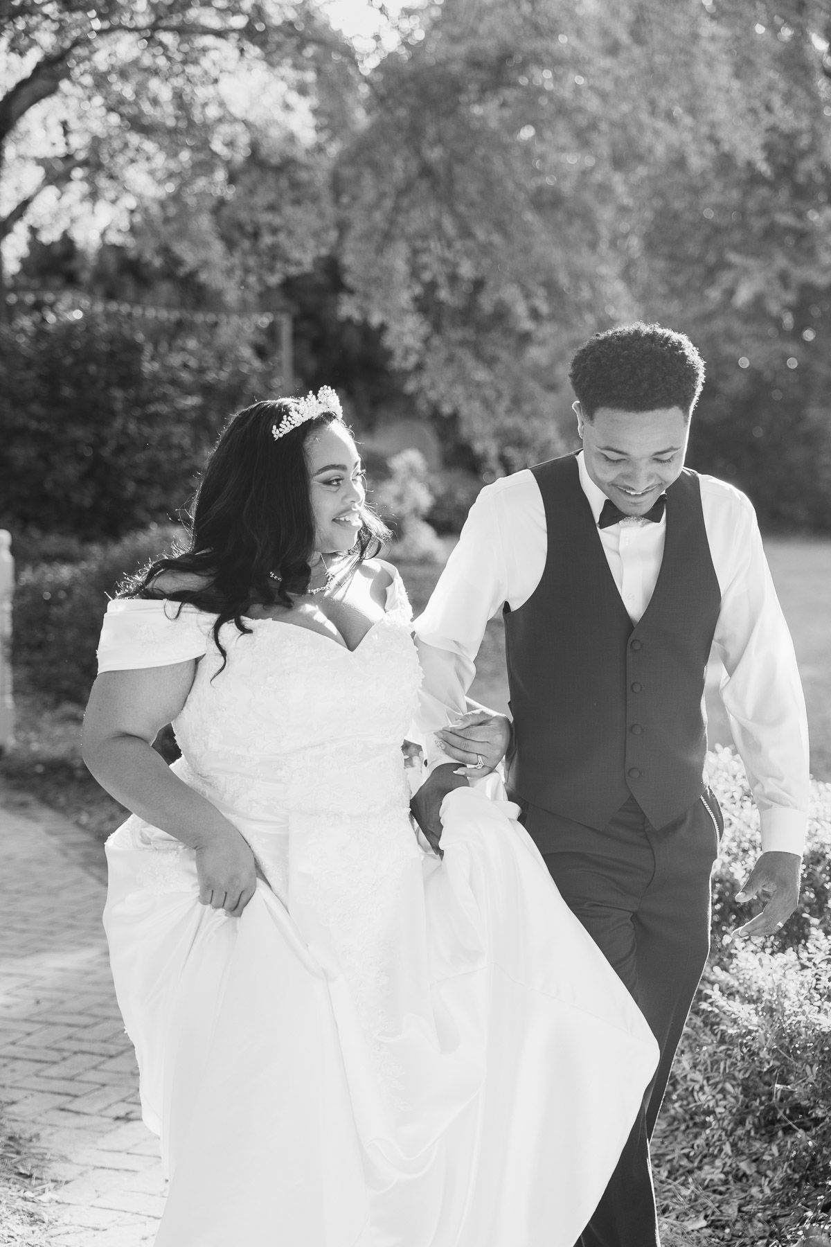 Black and white photo of a smiling bride and groom walking together outdoors on their wedding day.