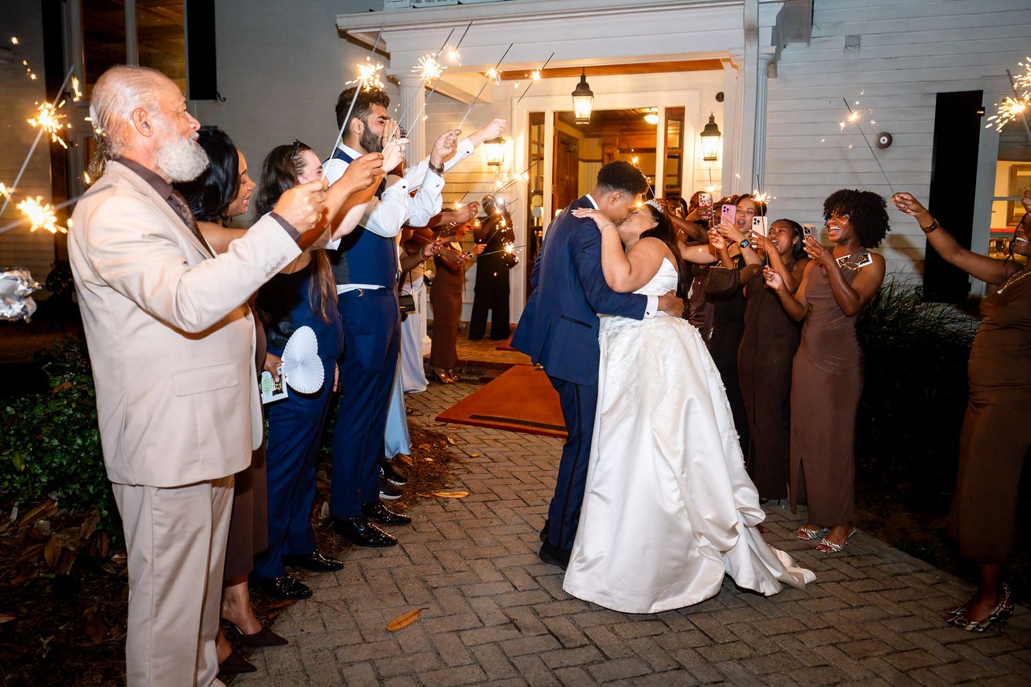 Newlyweds share a romantic kiss during a sparkler send-off surrounded by cheering wedding guests at Carl House wedding venue in Auburn Georg