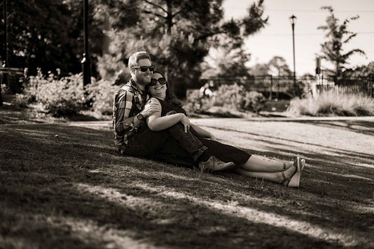 Couple sitting together on grass in a park, embracing in a romantic sepia-toned outdoor portrait photo.