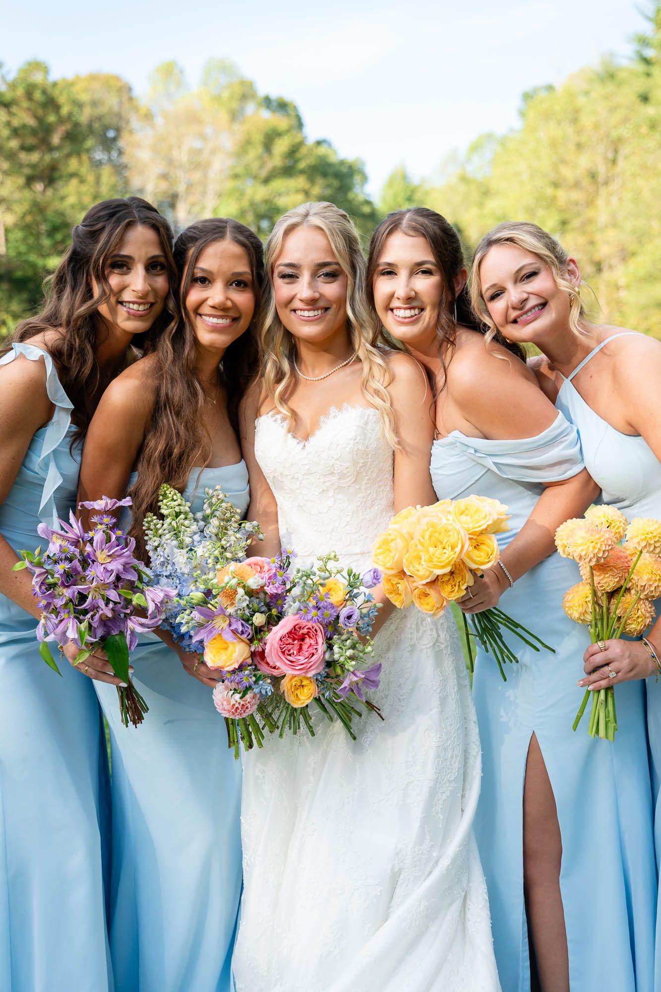 Bridesmaids in soft blue dresses smiling with the bride at a Georgia vineyard wedding