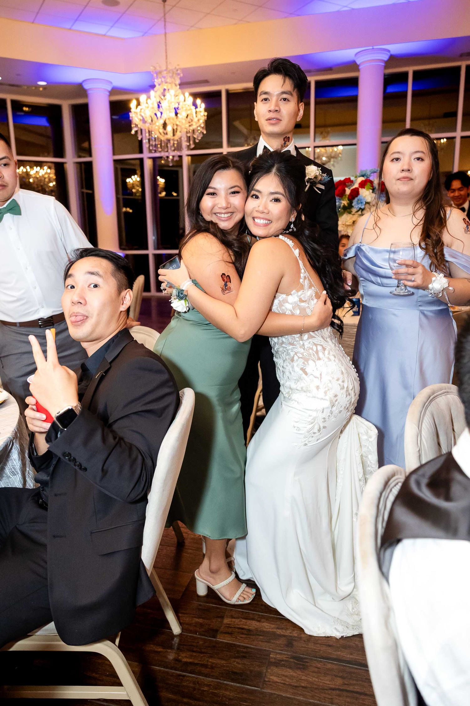Guests posing and hugging at an elegant wedding reception in a decorated ballroom with chandeliers.