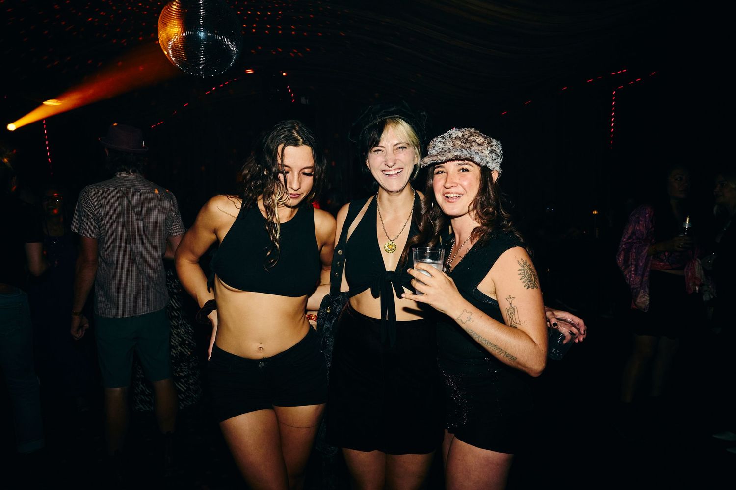 Group of people dancing and socializing in a dark nightclub setting with colorful lighting effects.