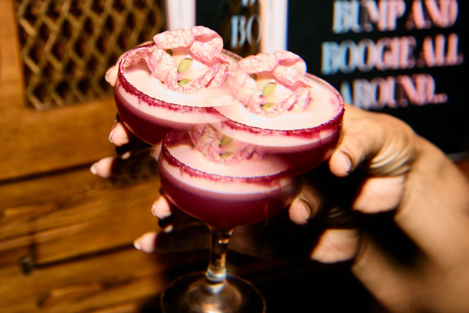Pink beverage in a stylish glass with sugar rim and decorative garnish.