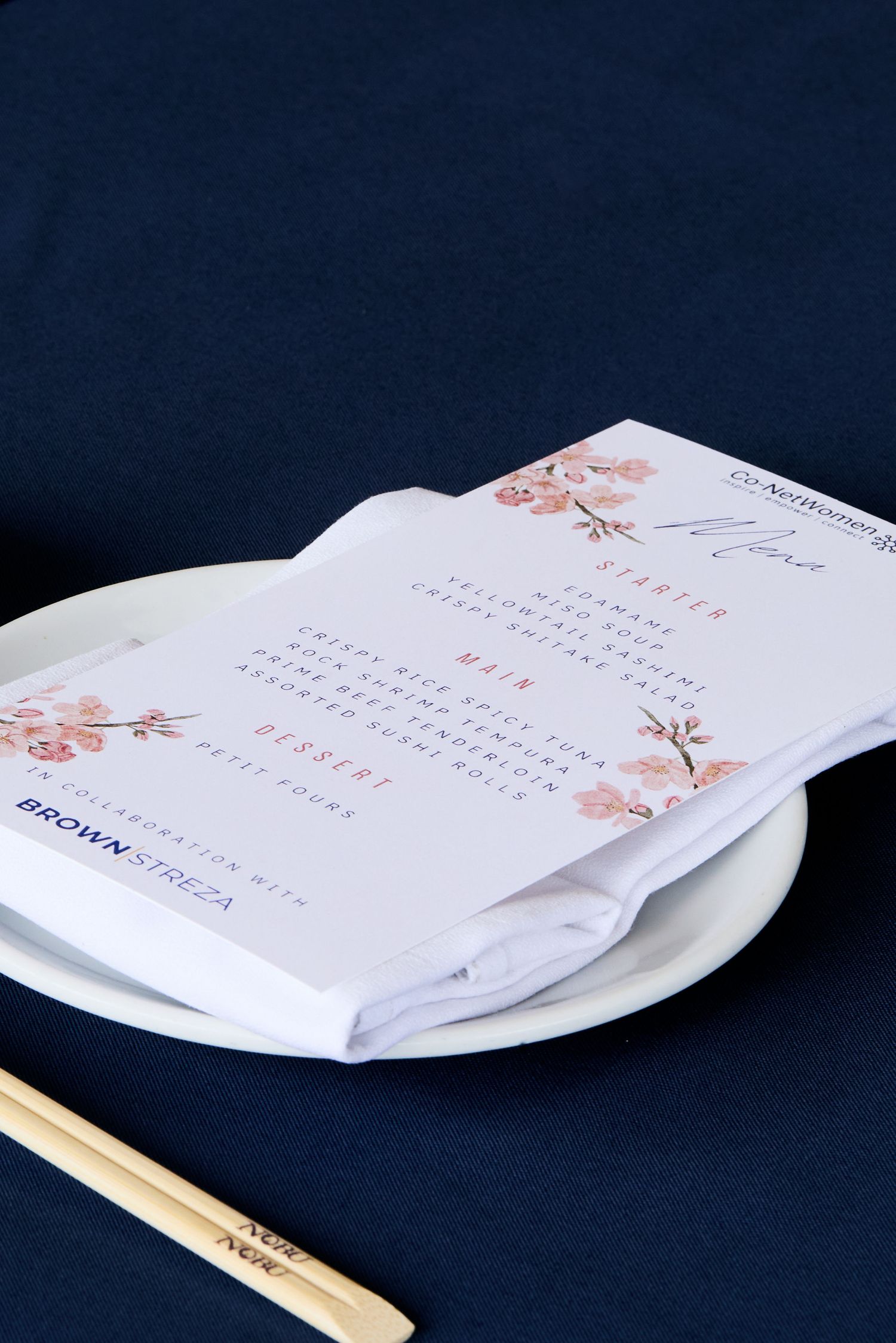 Calendar pages with delicate pink cherry blossom designs rest on a white plate against a navy blue background.