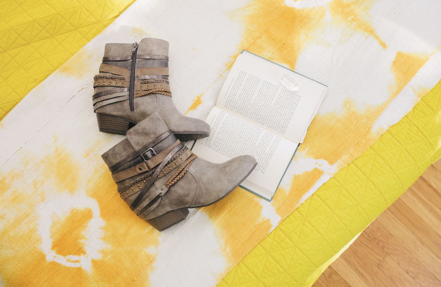 Gray suede ankle boots with buckle details on yellow and white patterned surface.