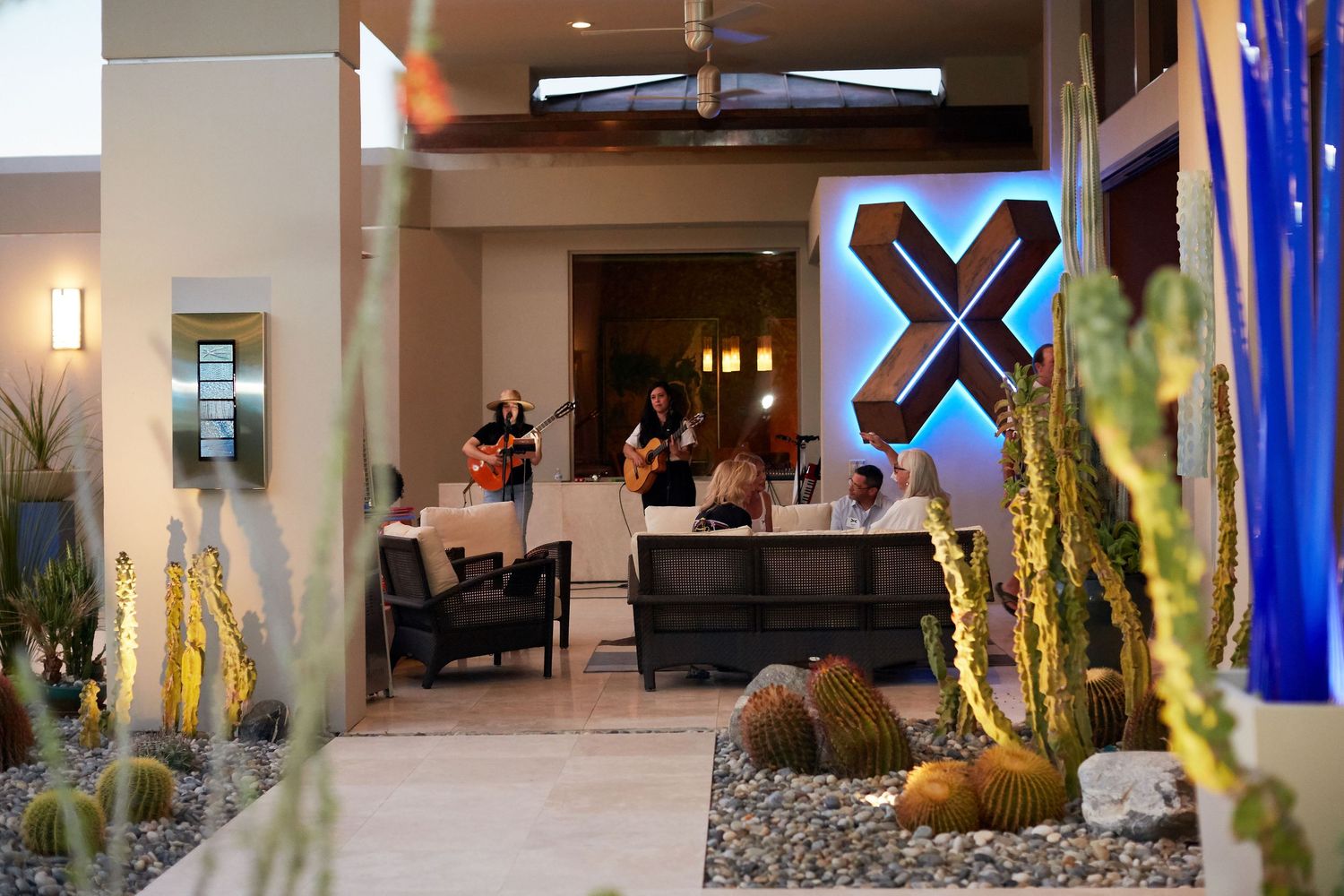Musicians perform in a modern hotel lobby lounge with desert landscaping and contemporary decor.