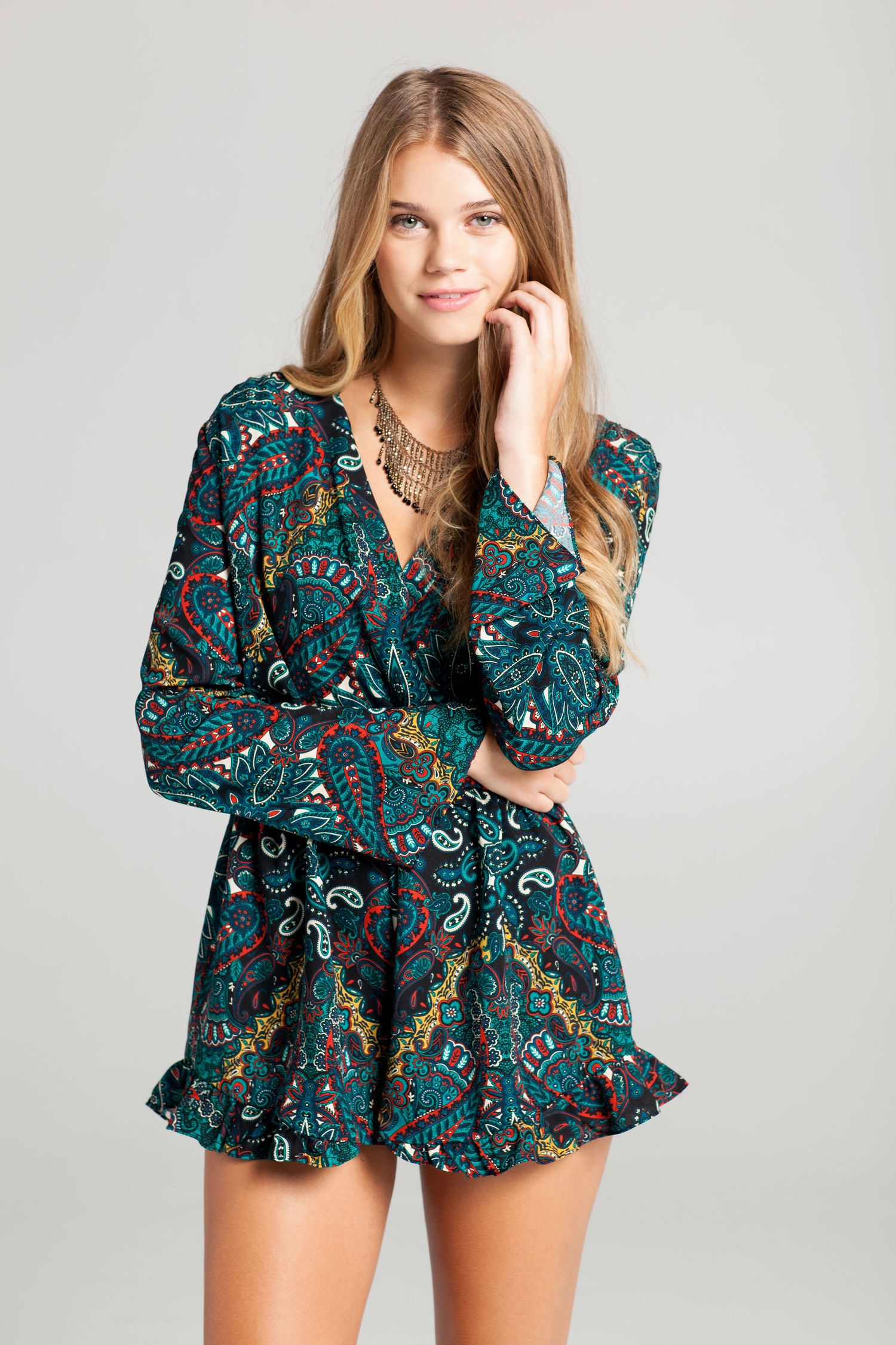 Fashion model in teal paisley print romper with long sleeves against grey background.