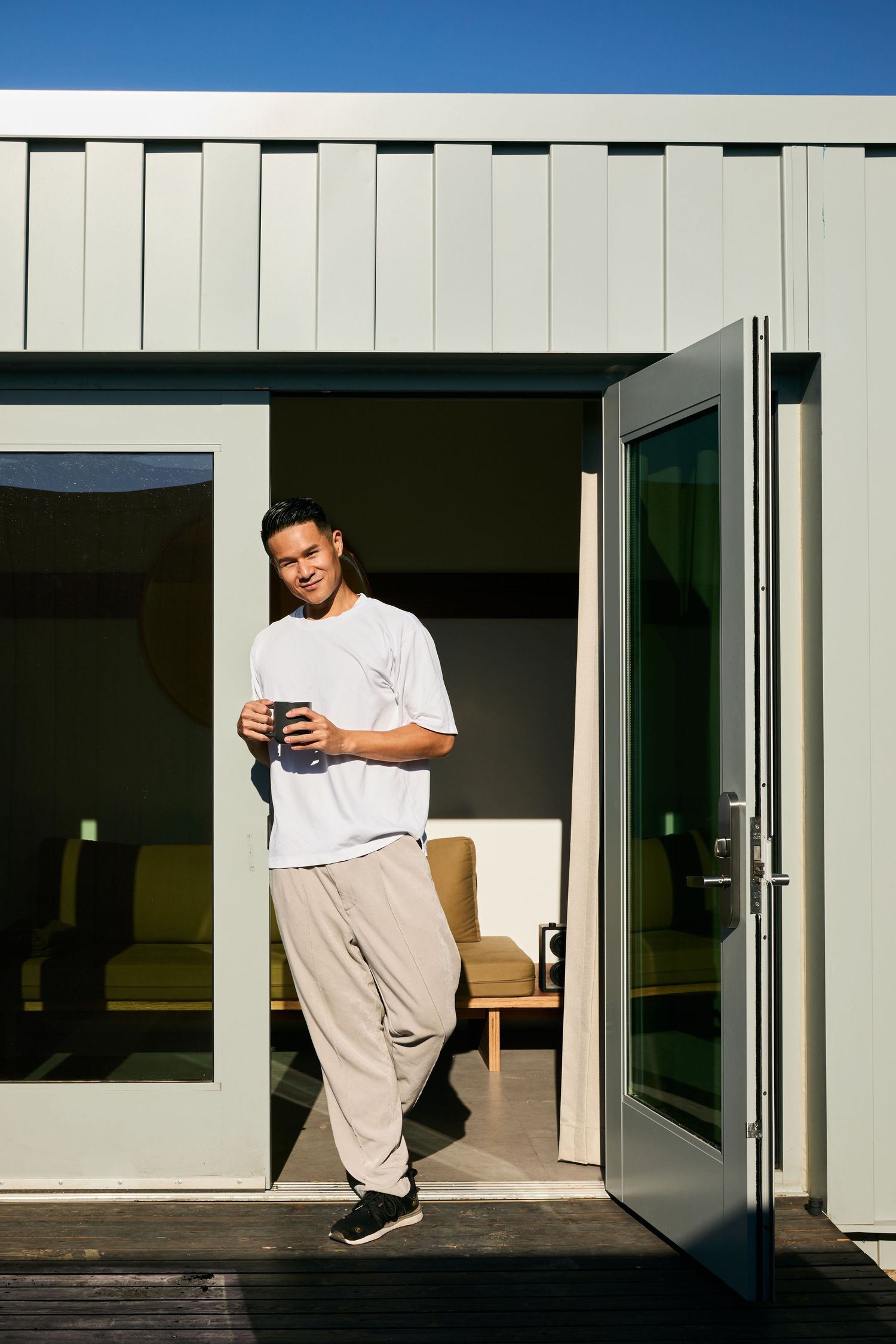 Someone in a white t-shirt and khaki pants checks their phone while standing in a doorway on a sunny day.