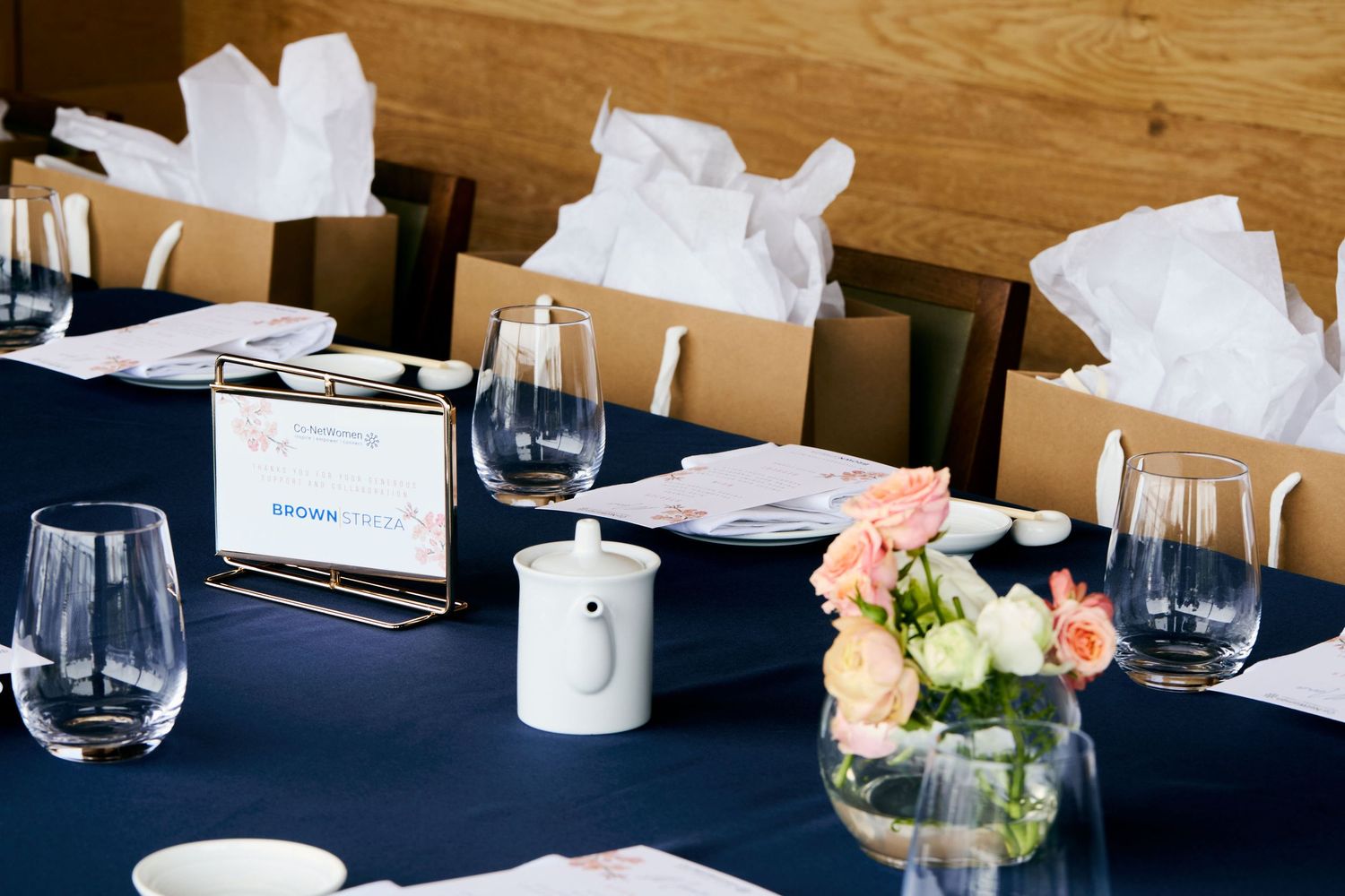 Elegant table setting with navy tablecloth, wine glasses, name cards, and pink floral centerpiece in glass vase.