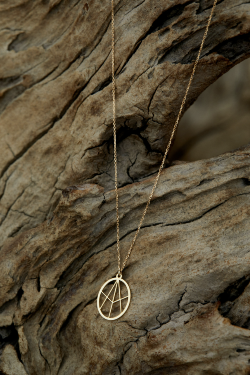 Gold geometric pendant necklace photographed against textured rock surface.