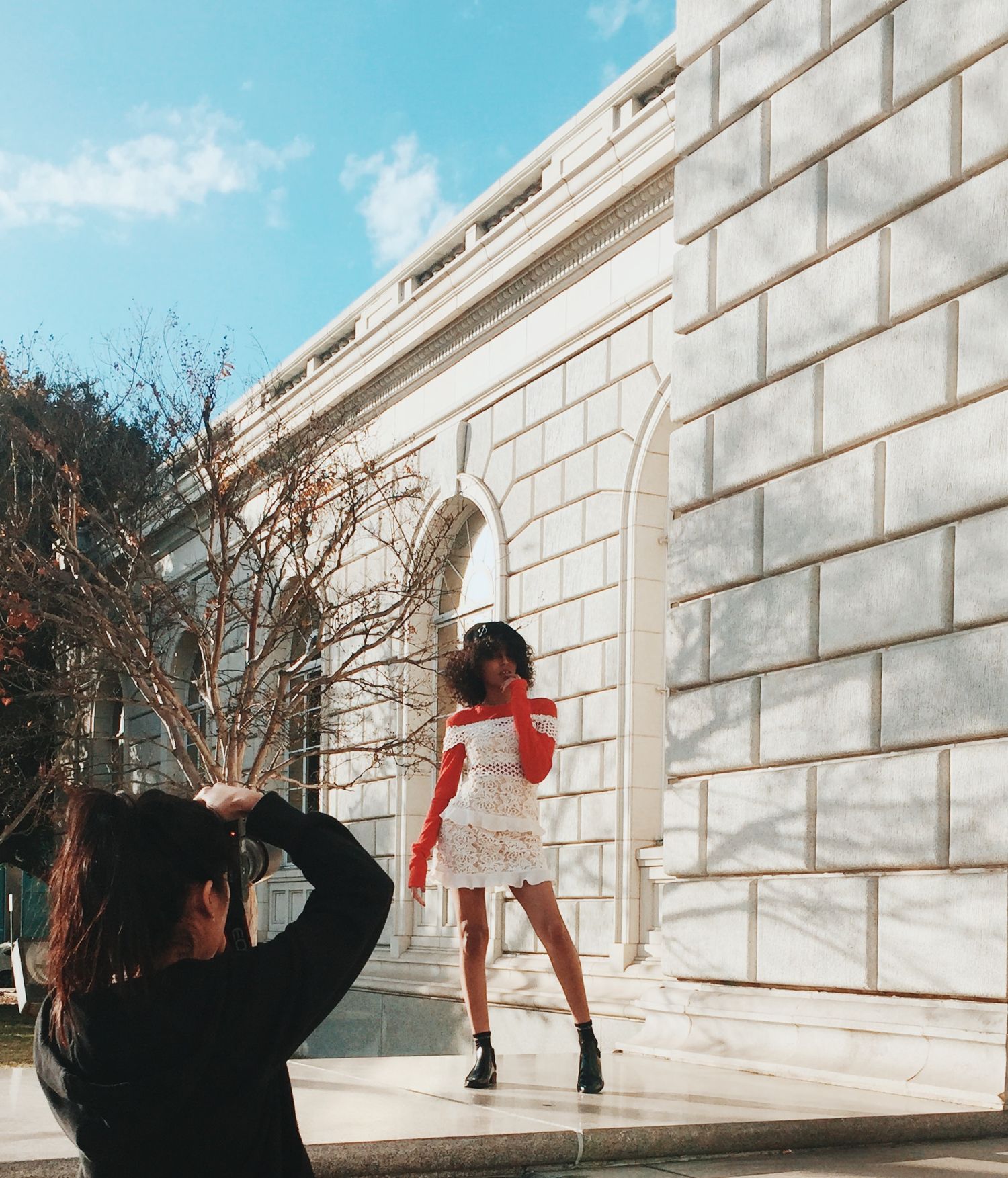 A person in red attire performs a dynamic dance sequence against a white stone wall on a sunny day.