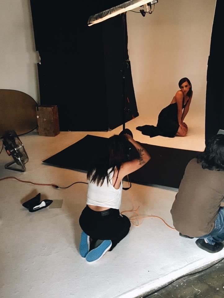 Behind-the-scenes photo shoot in a studio with lighting equipment and a white backdrop setup in progress.