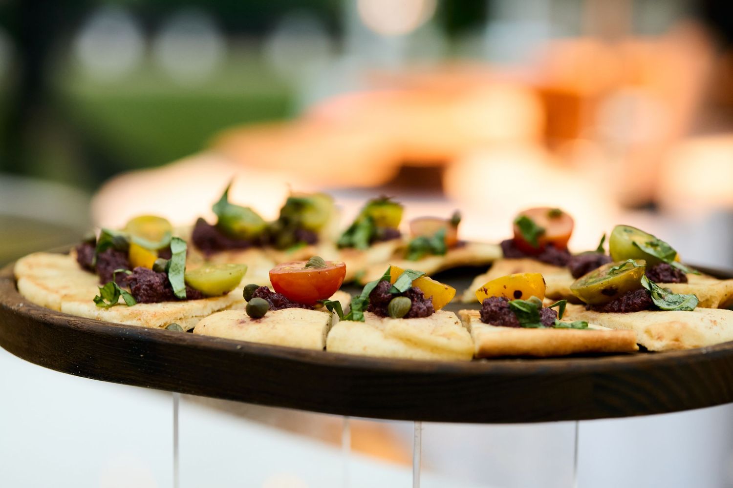 Close-up of gourmet appetizers with colorful toppings served on a rustic wooden board in soft natural lighting.
