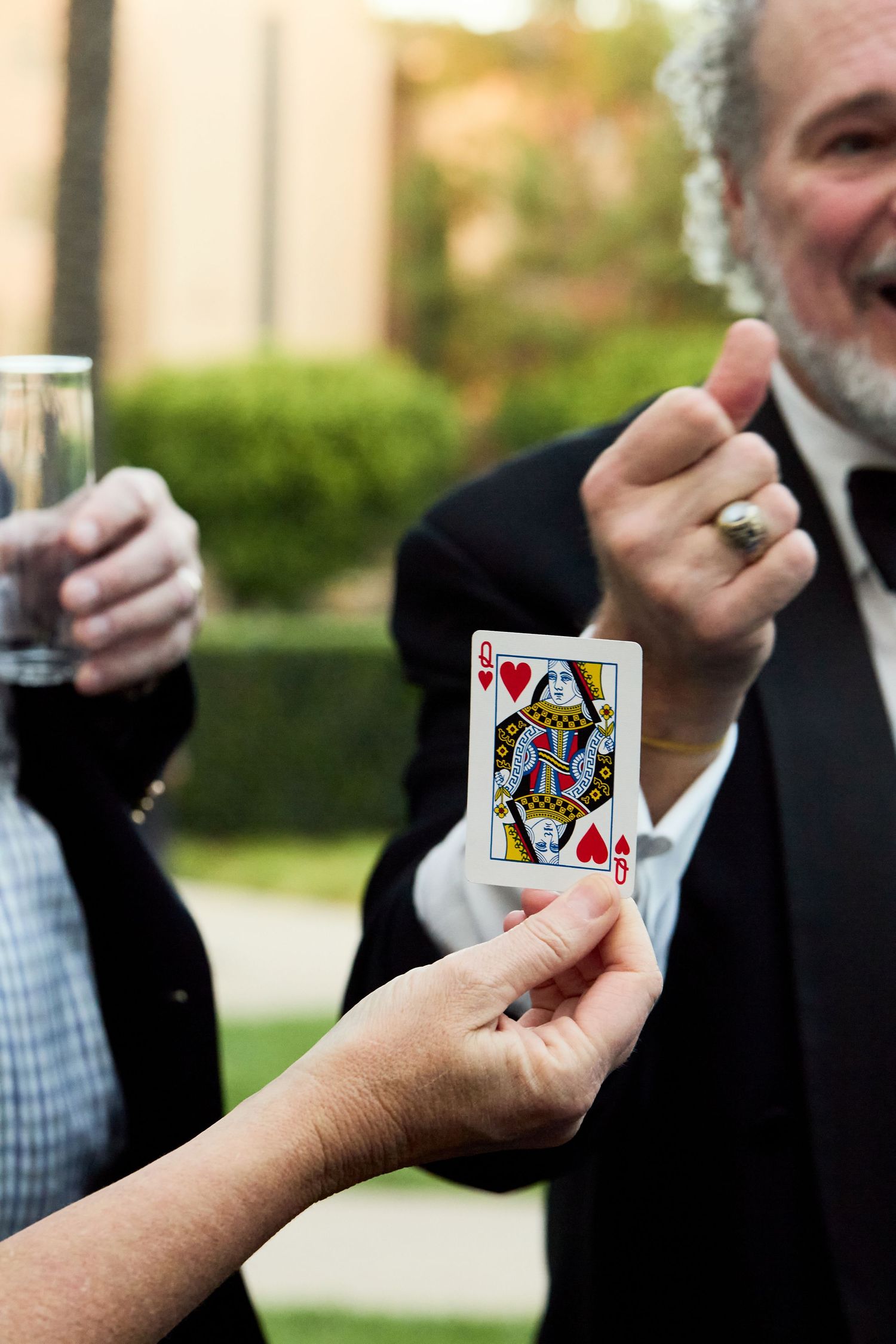 A row of hands holding playing cards outdoors with a King of Hearts card visible in focus.