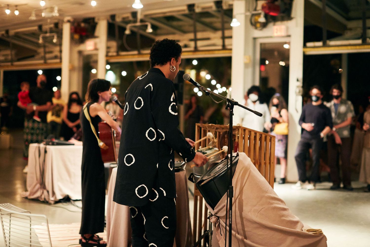 A musician in black patterned clothing performs at an elegant indoor venue with soft lighting and guests in the background.