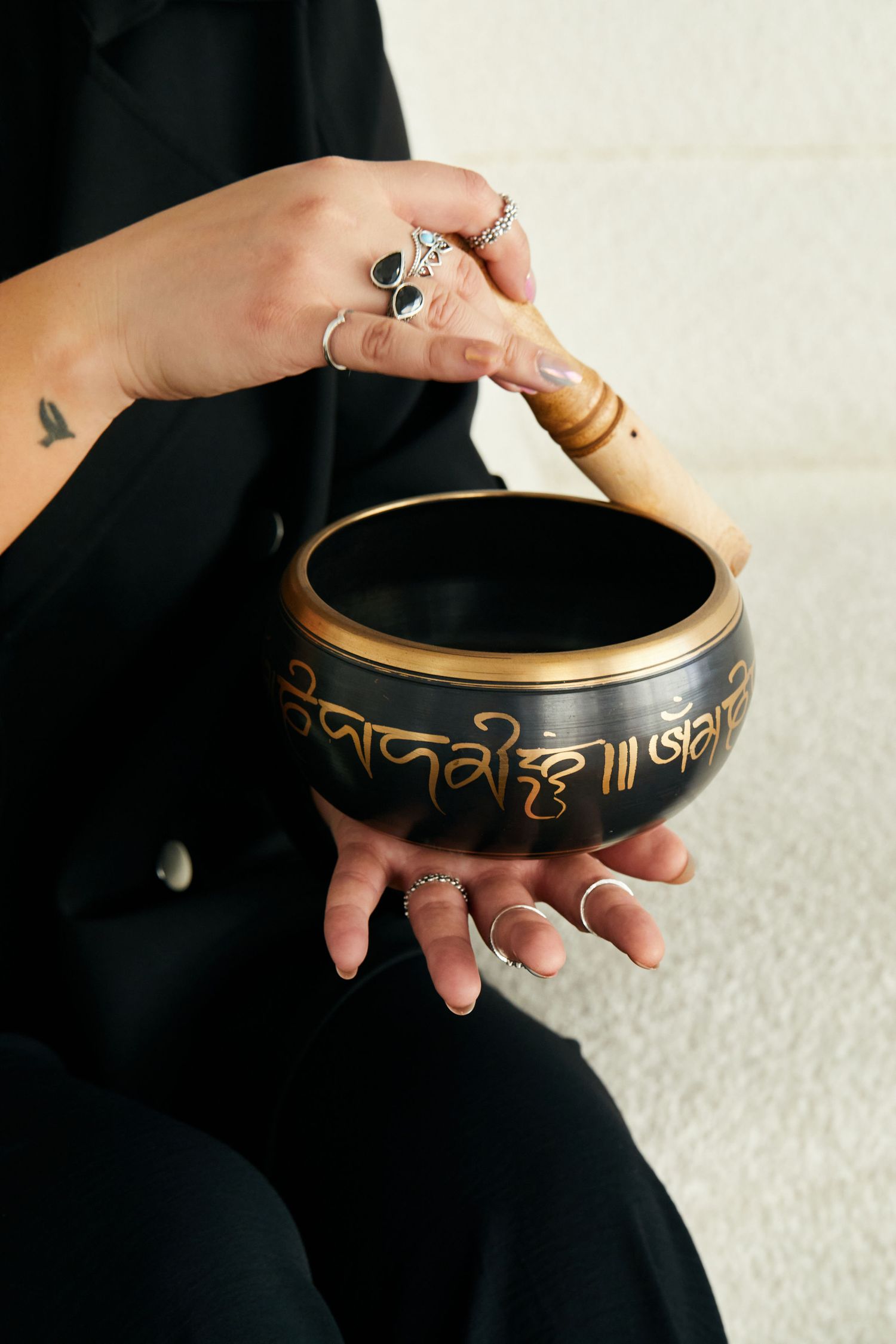 Hands with silver rings playing a Tibetan singing bowl with a wooden mallet for meditation.