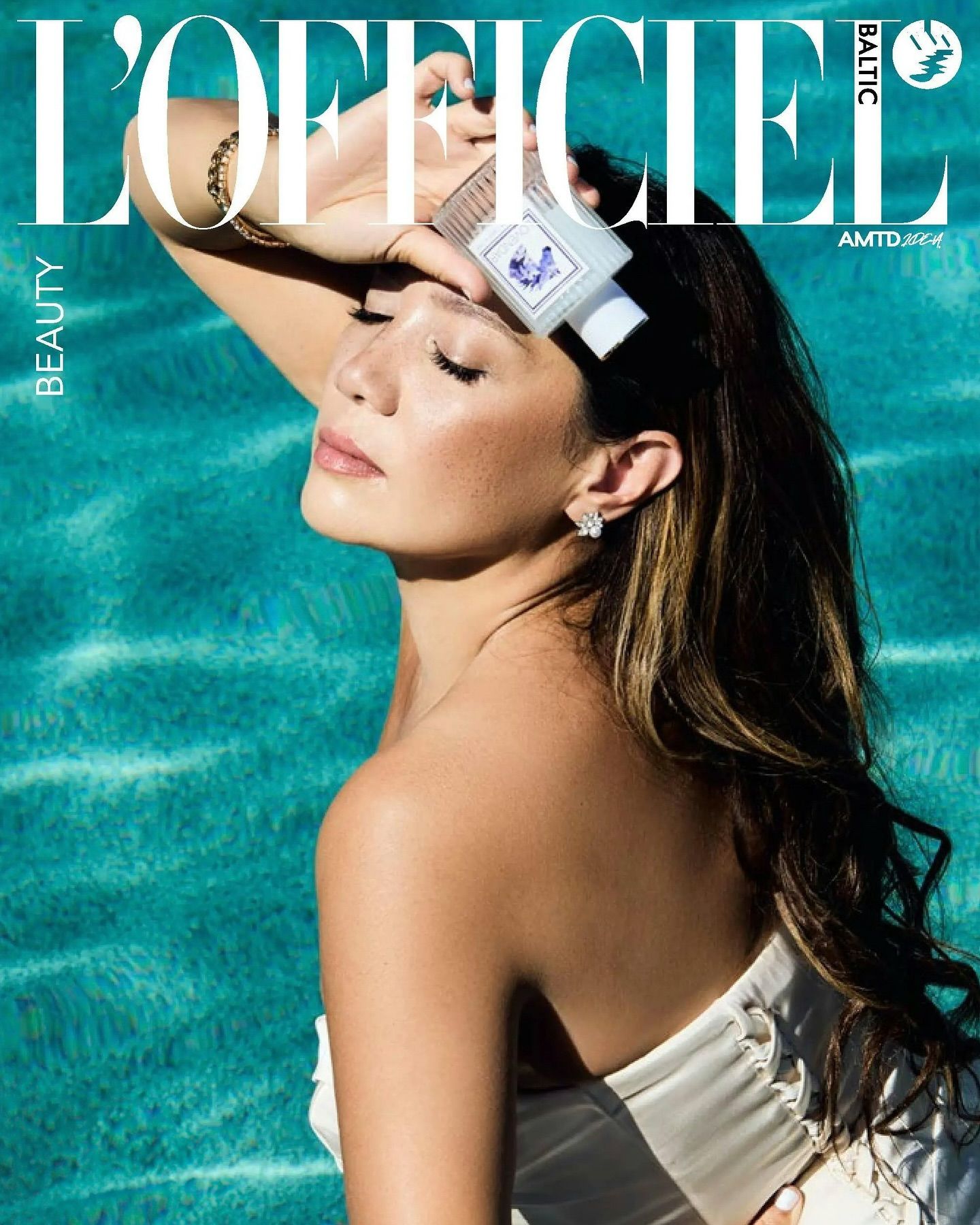 Fashion model in white swimwear poses against turquoise water background for magazine editorial shoot.