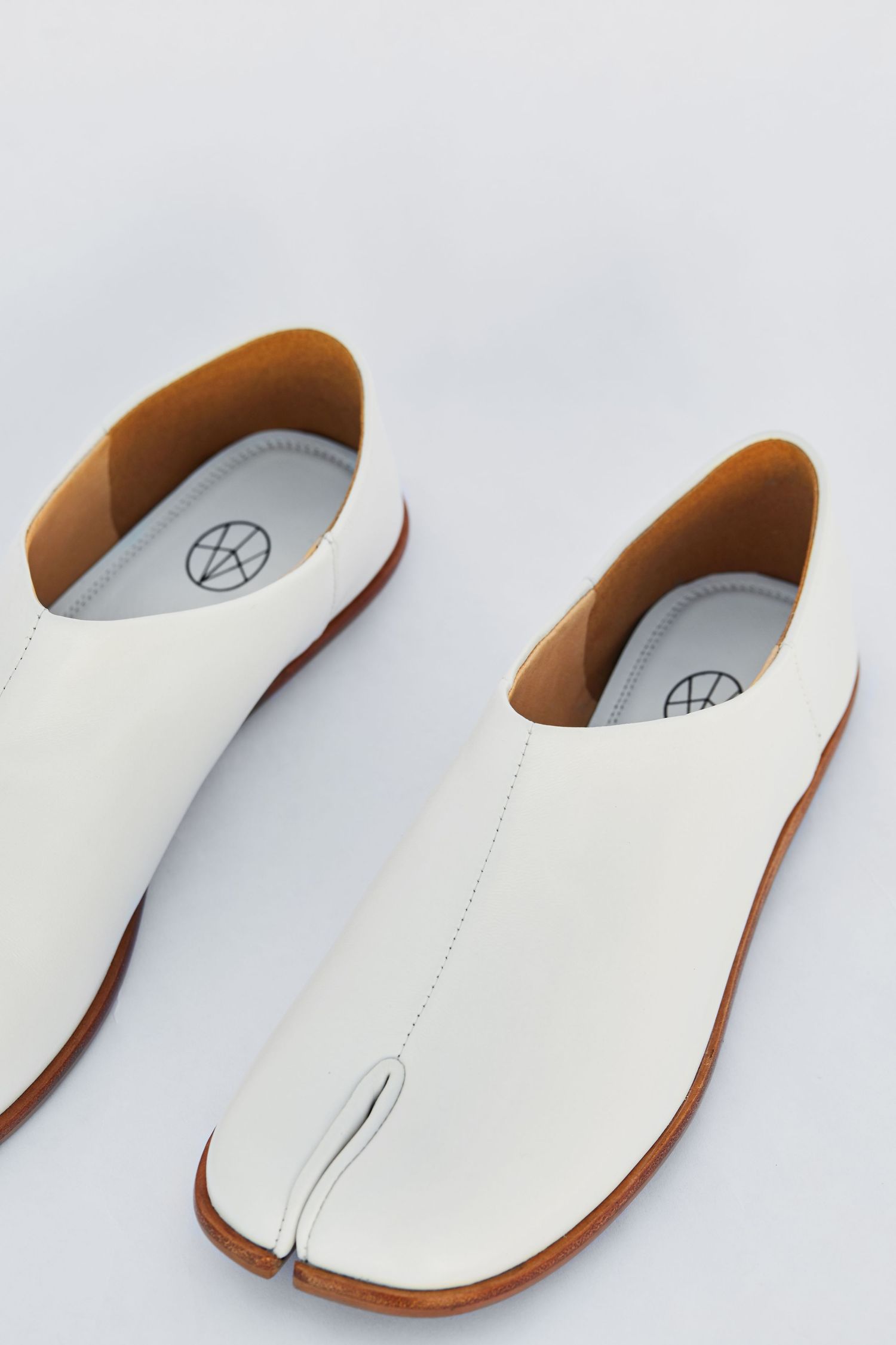 Minimalist white leather tabi-style shoes with split toe design on light background.