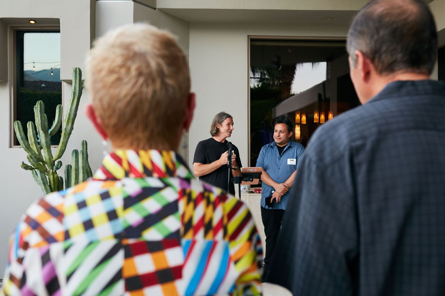 People stand in a doorway entrance while being greeted by others wearing colorful patterned clothing.