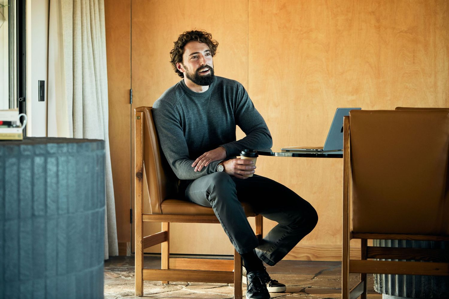 Person wearing a navy sweater sits casually on a wooden chair in a room with beige walls.