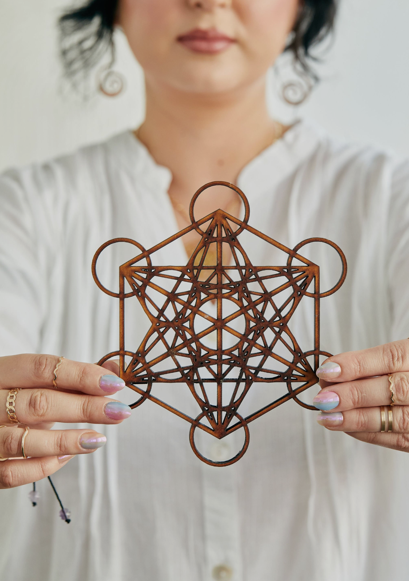 Hands holding geometric copper wire sculpture in sacred geometry pattern.