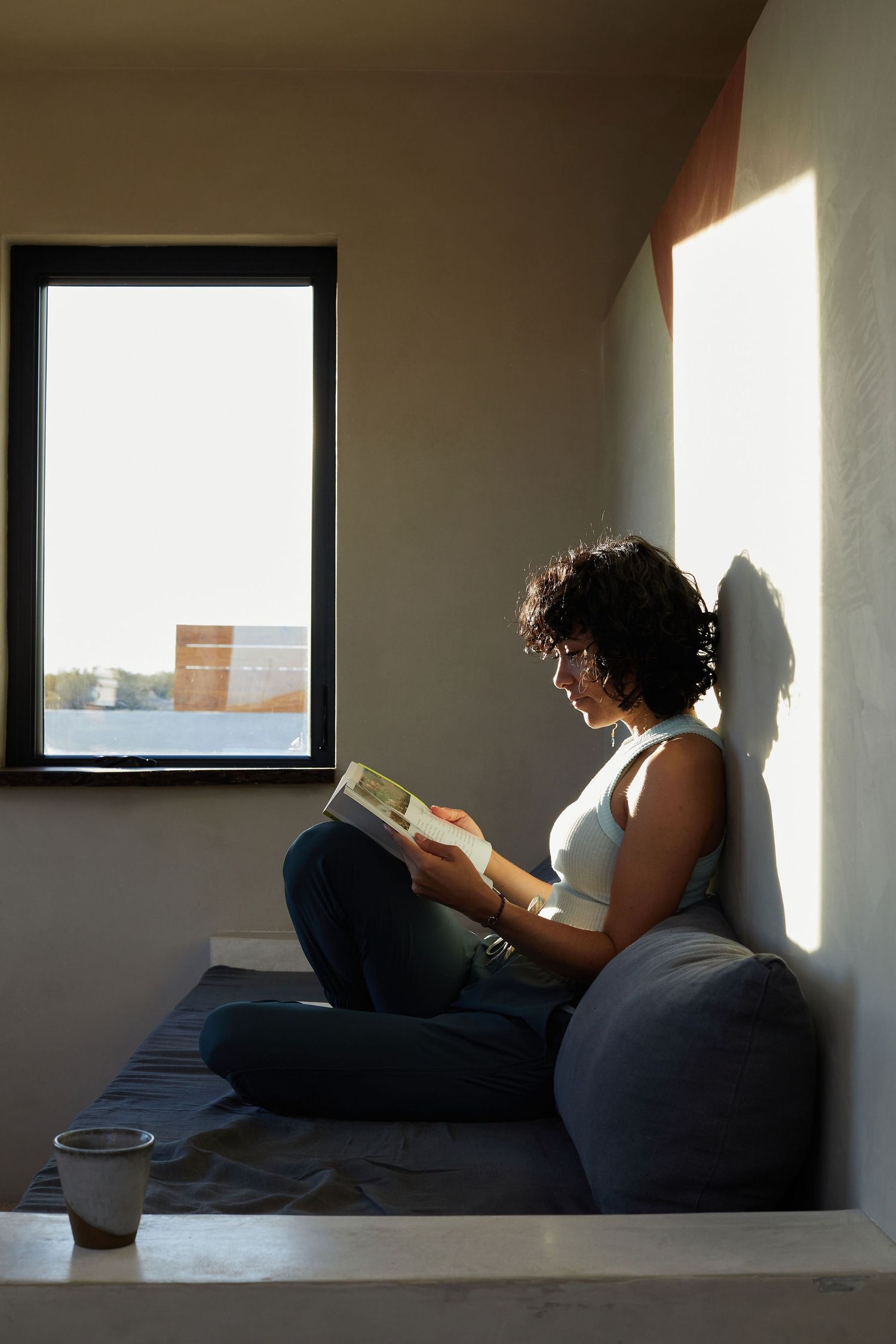 Person reading book in cozy window nook with natural lighting.